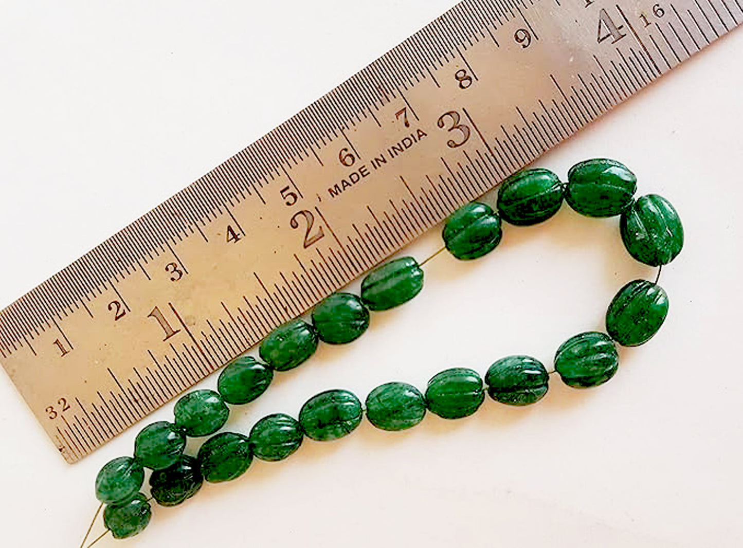 A ruler measures the emerald oval gemstone.
