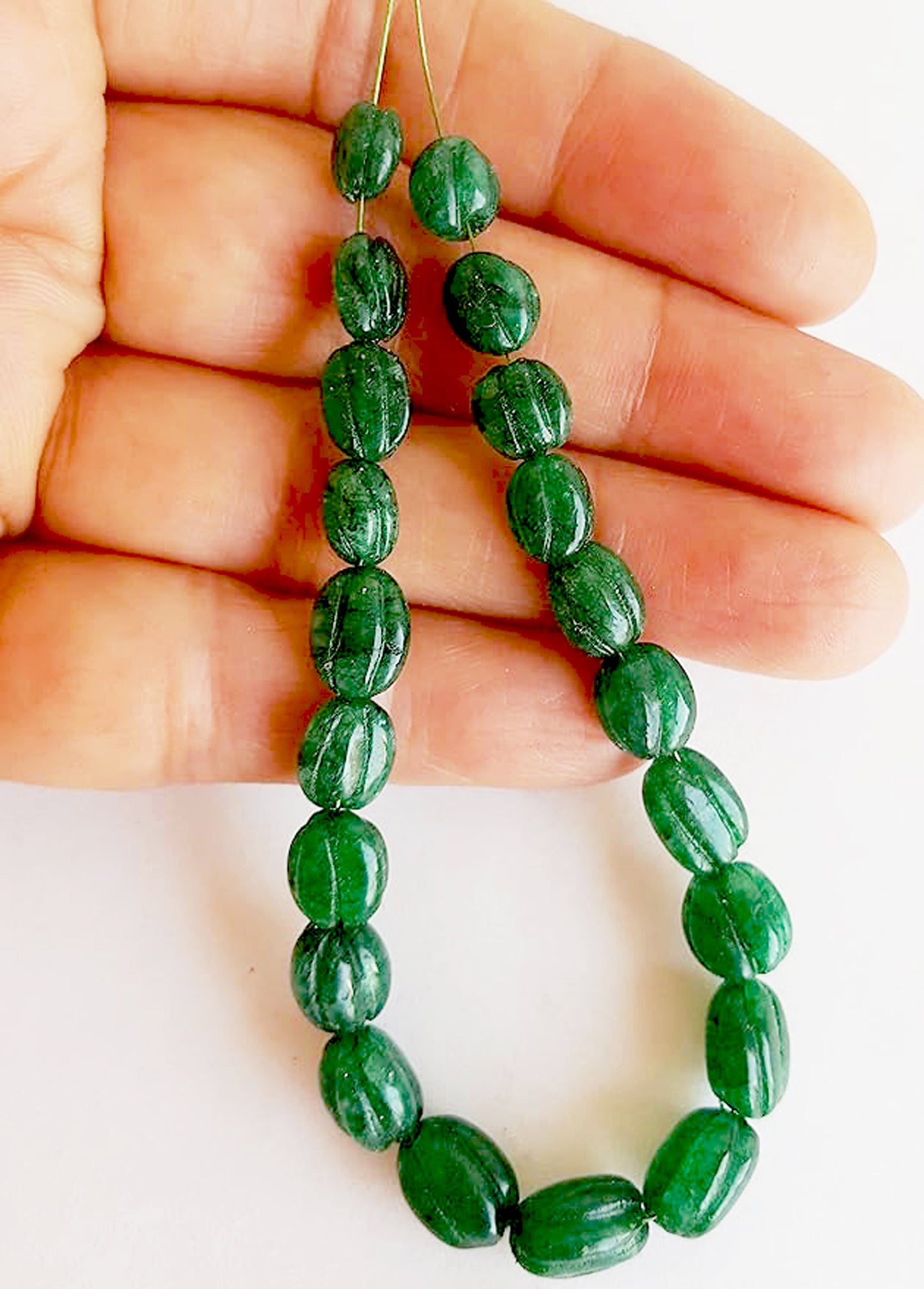 A person holds delicate strands of emerald beads, showcasing their smooth design.