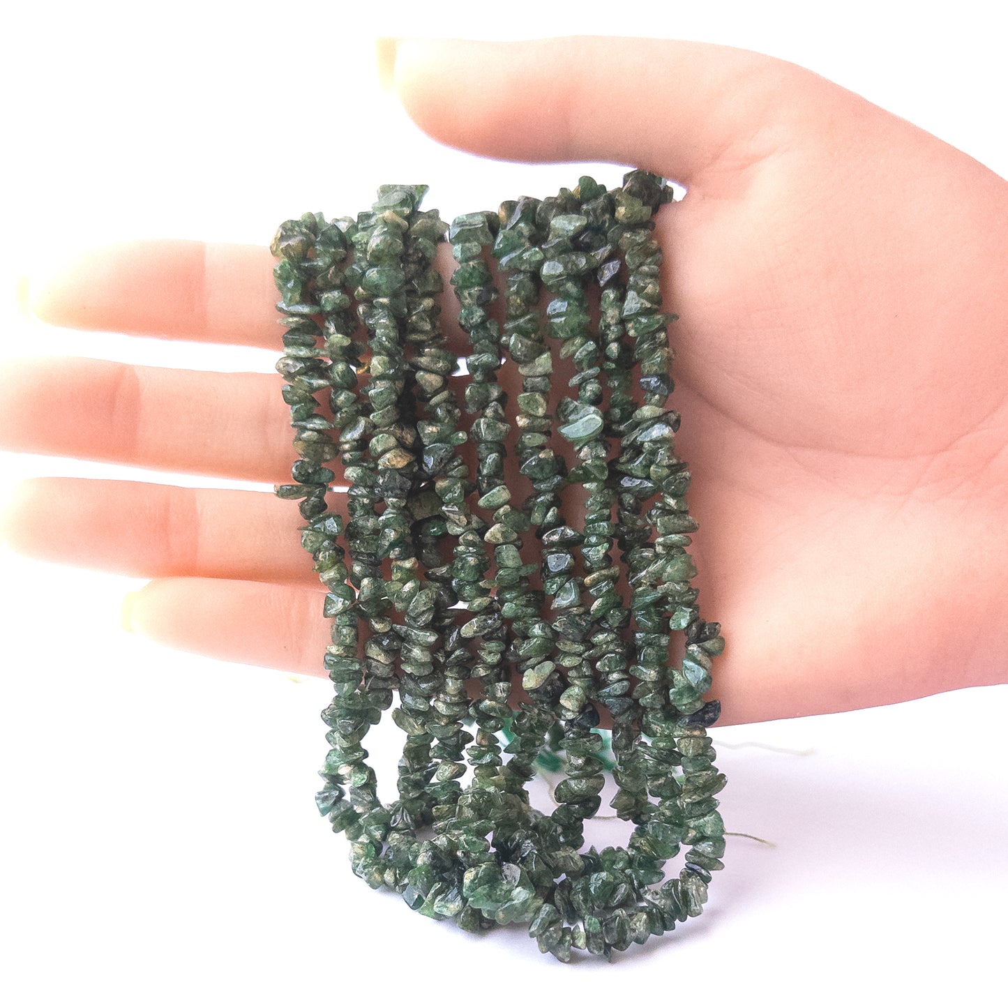 A person holds delicate strands of Shaded Emerald chip beads, showcasing their organic design.