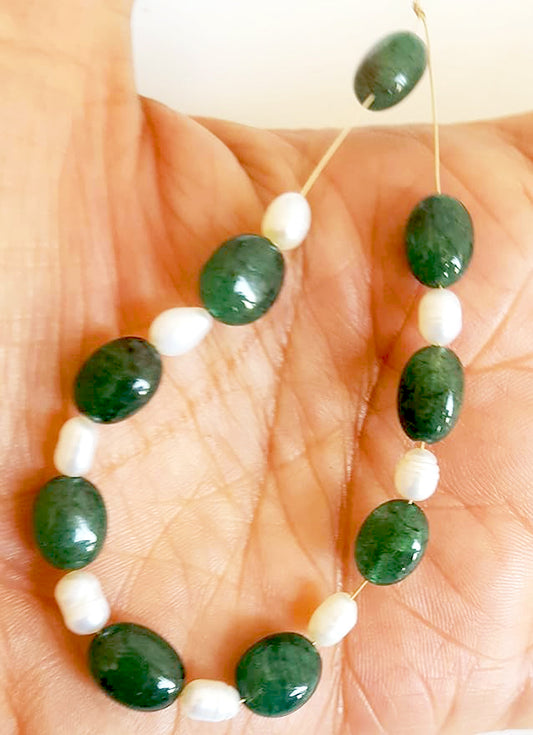 A person holds delicate strands of emerald and pearl beads, showcasing their smooth design.