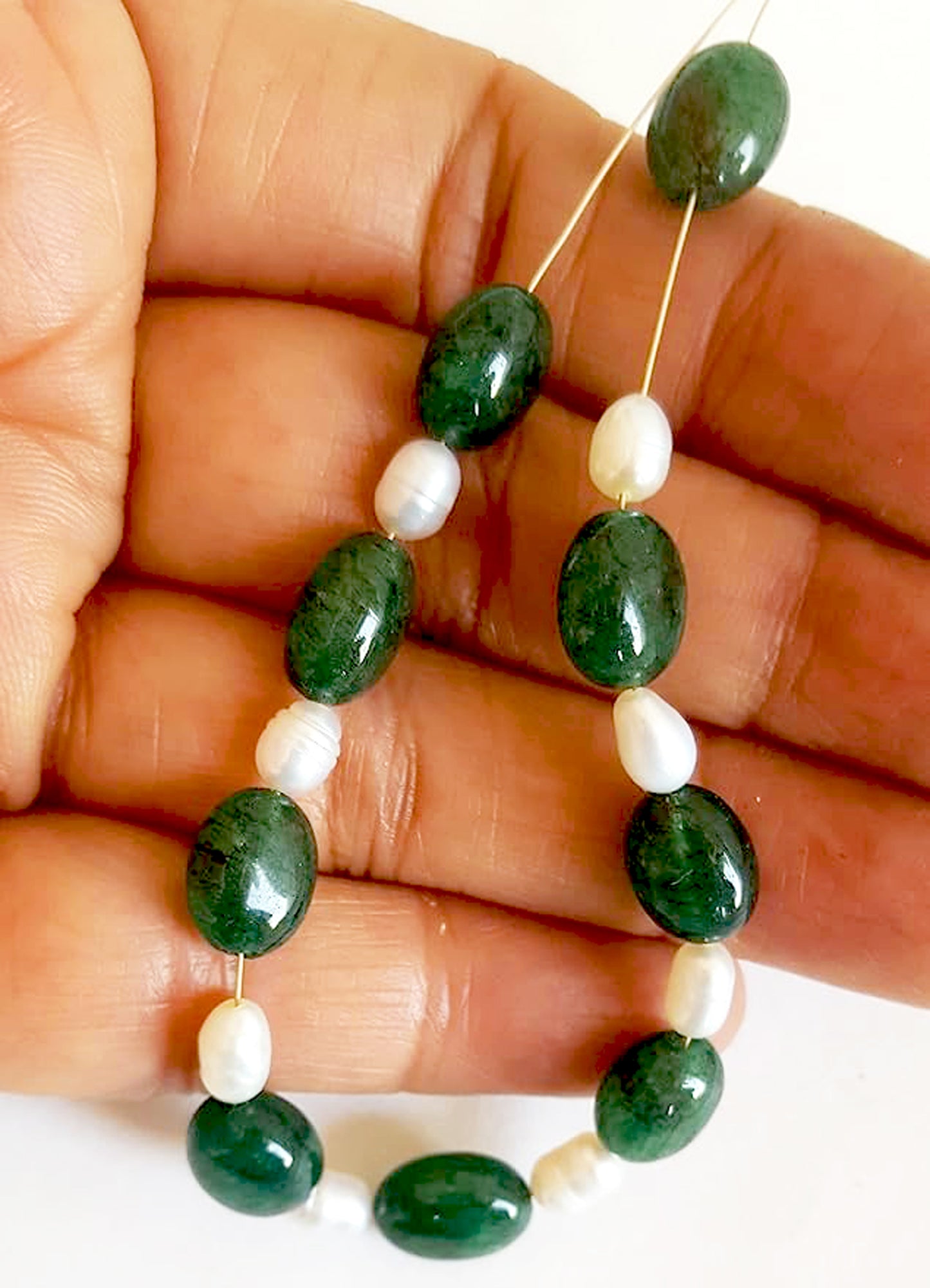 A person holds delicate strands of emerald and pearl beads, showcasing their smooth design.