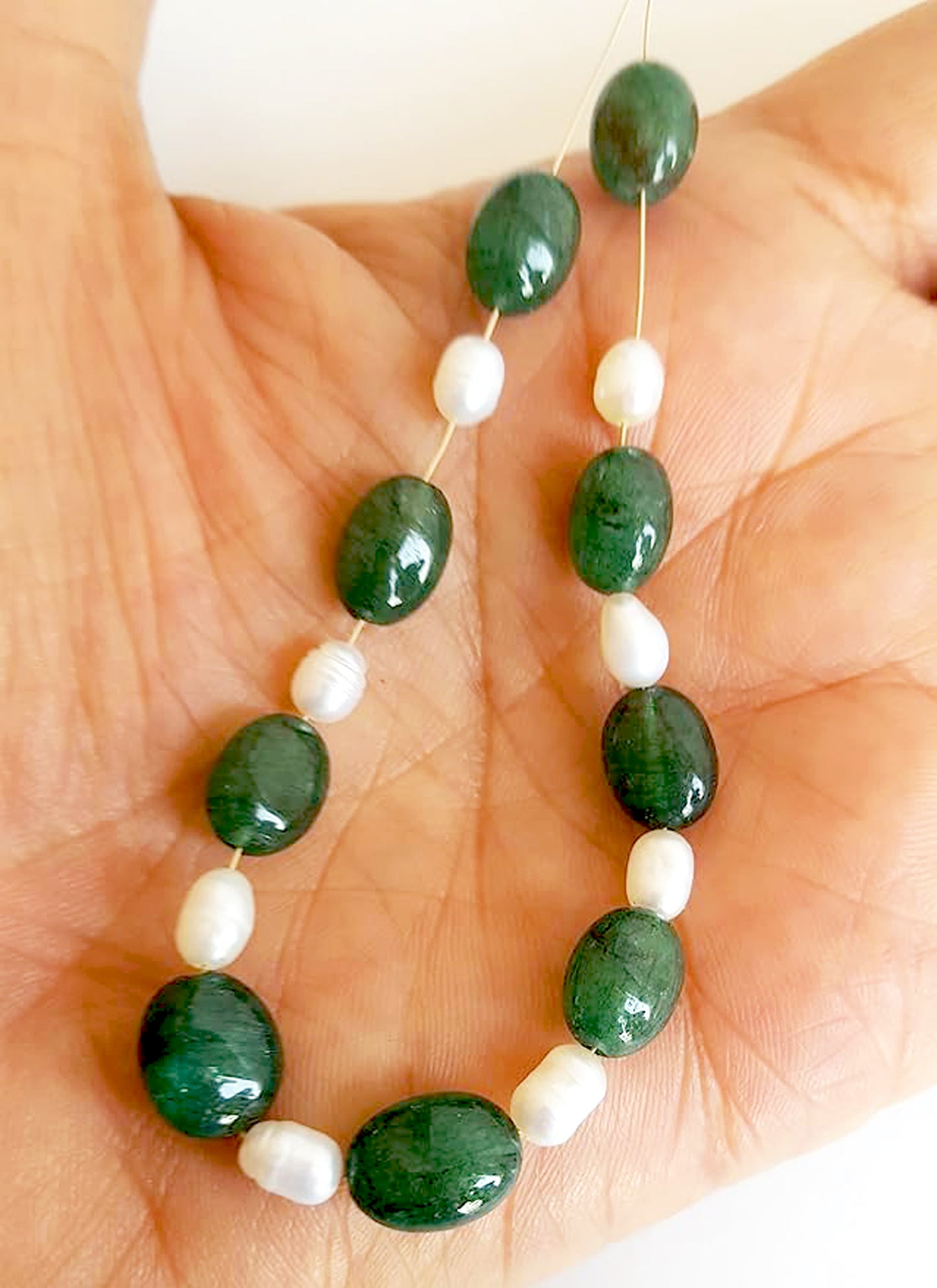 A person holds delicate strands of emerald and pearl beads, showcasing their smooth design.