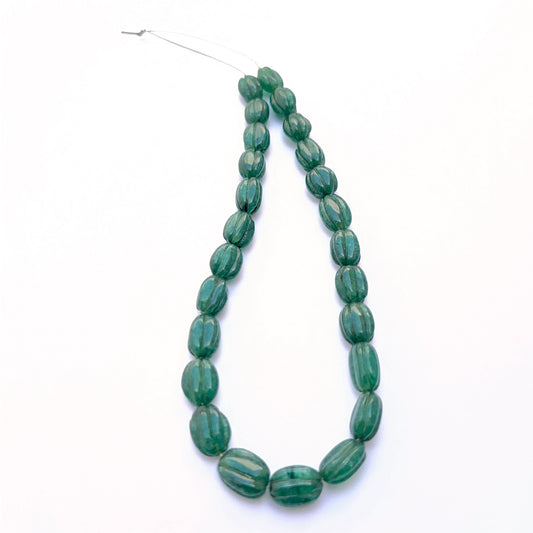 Close‑up of carved oval emerald beads arranged in a finished emerald necklace.