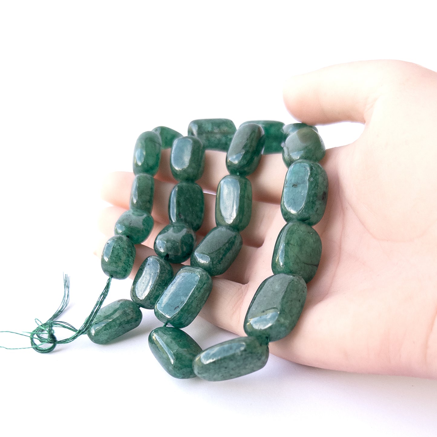 A person holds delicate strands of Emerald beads, showcasing their smooth tumble design.