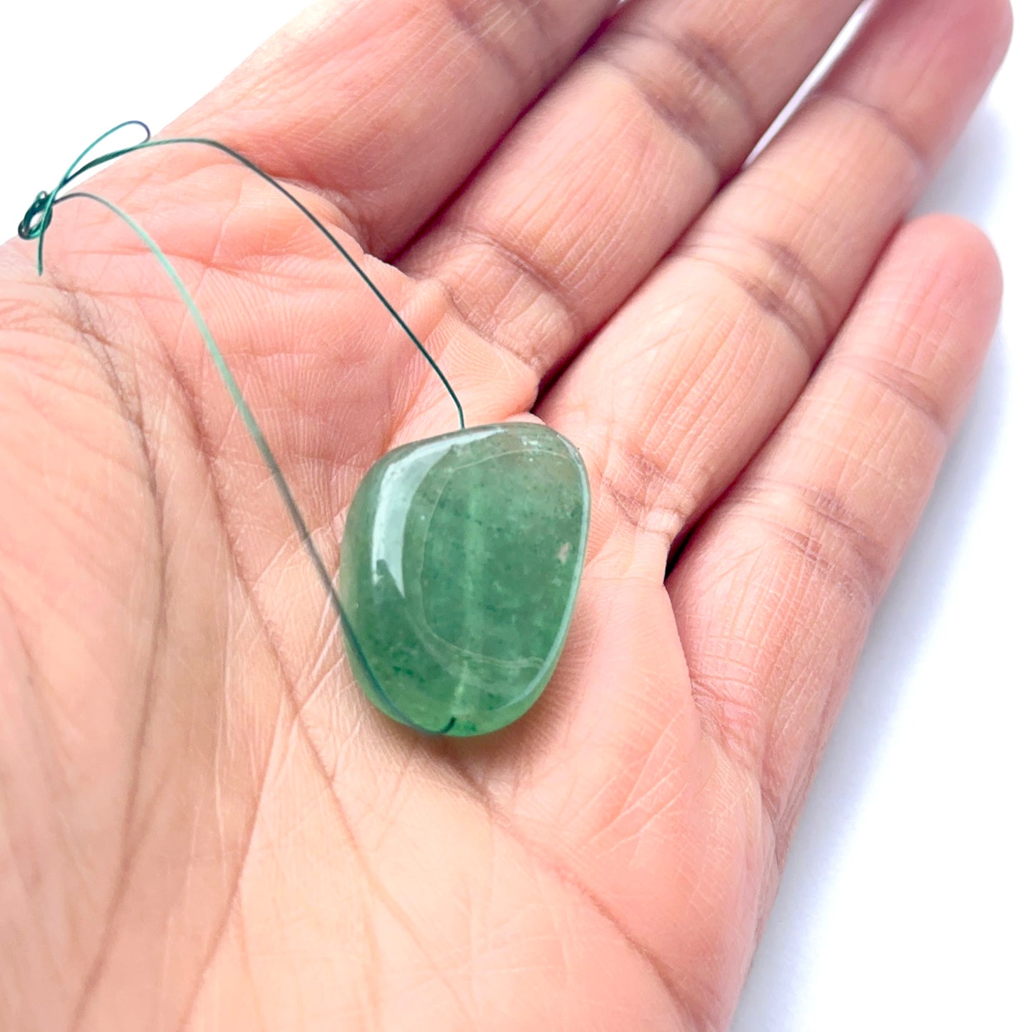 A person holds a single emerald tumble bead, showcasing its smooth drilled design.