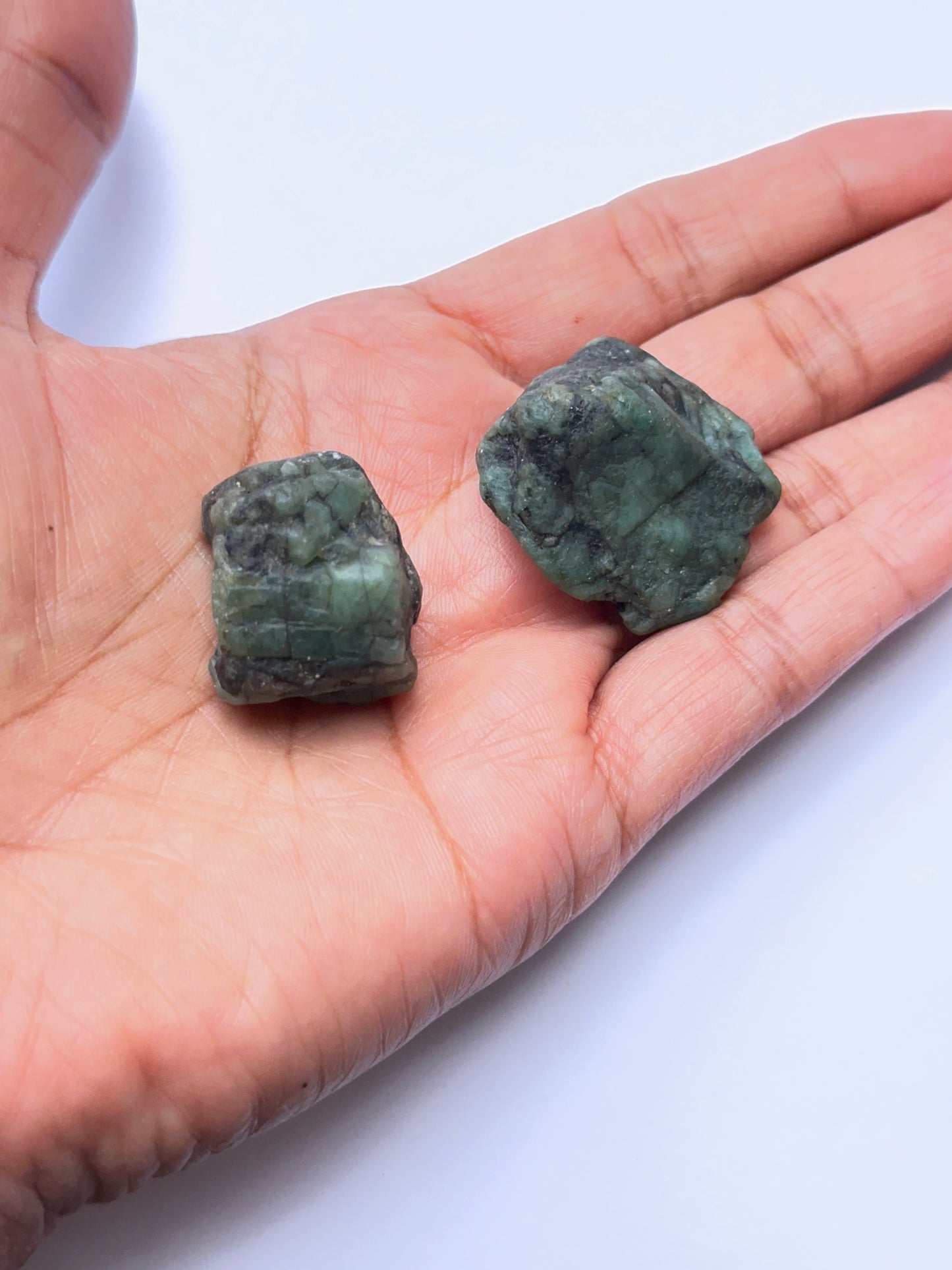 A person's hand shows close‑up of emerald rough stone highlighting raw structure and vibrant green colour.