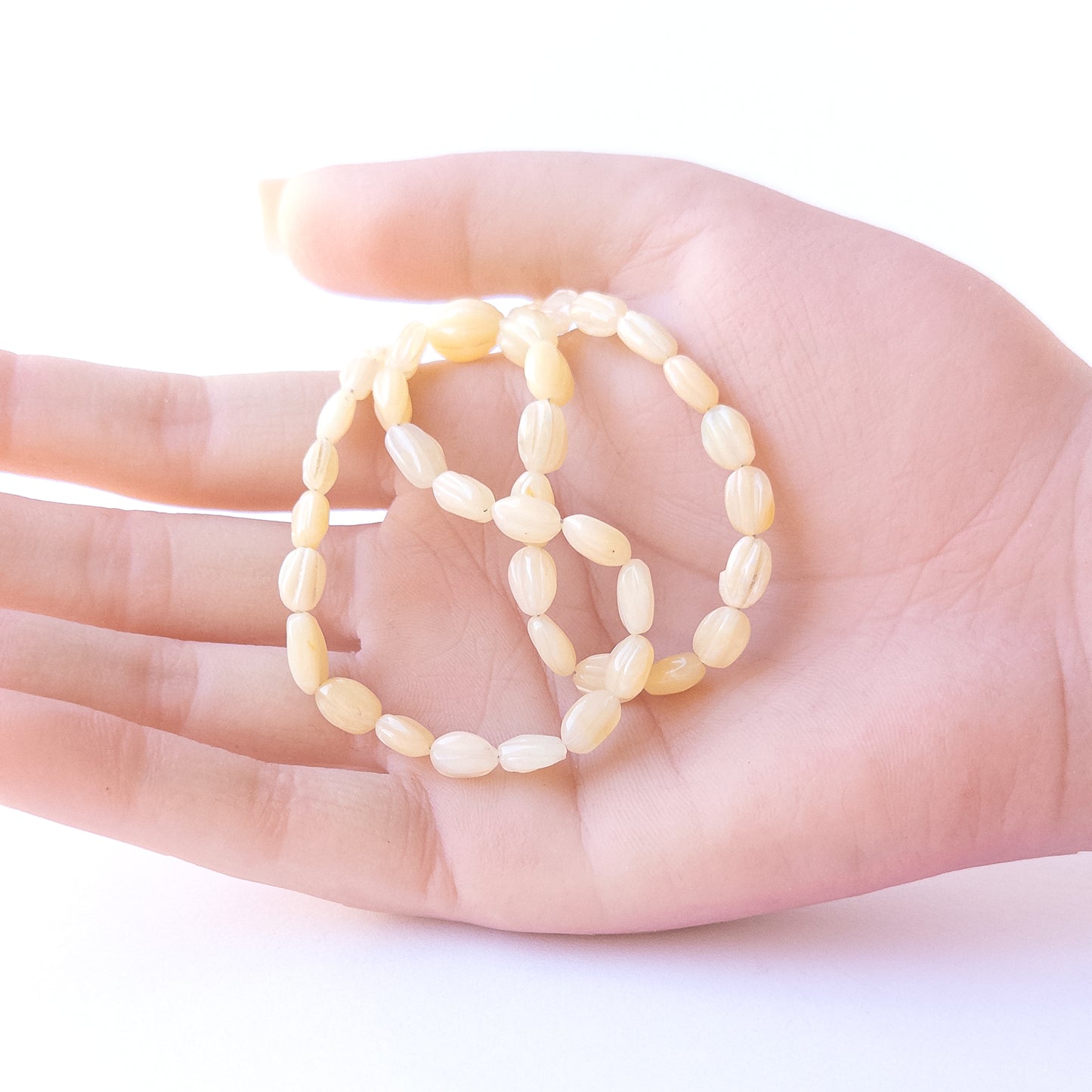 A person holds delicate strands of Ethiopian Opal carved oval beads, showcasing their carved design.