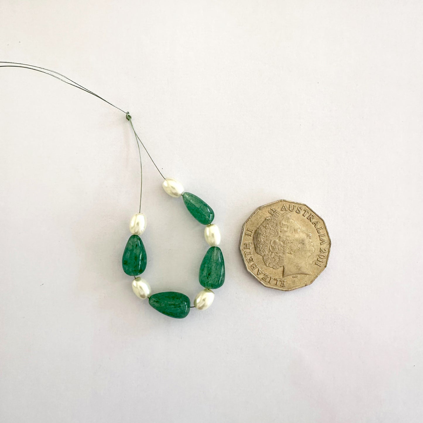 Close-up of emerald bead sand white pearls next to a Australian 50 cents coin to showcase the scale.