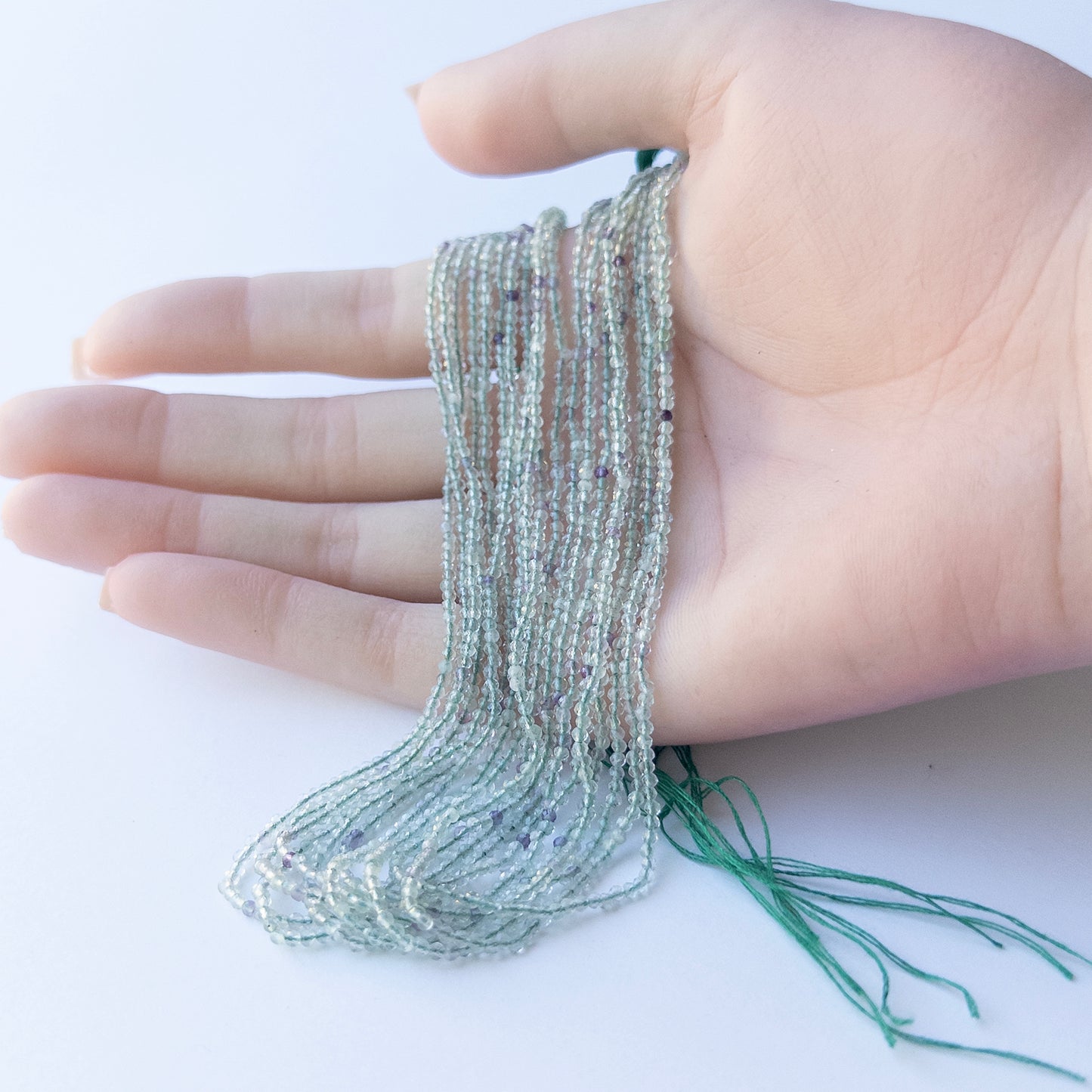 A person holds delicate strands of Fluorite beads, showcasing their Faceted Rondelle design.