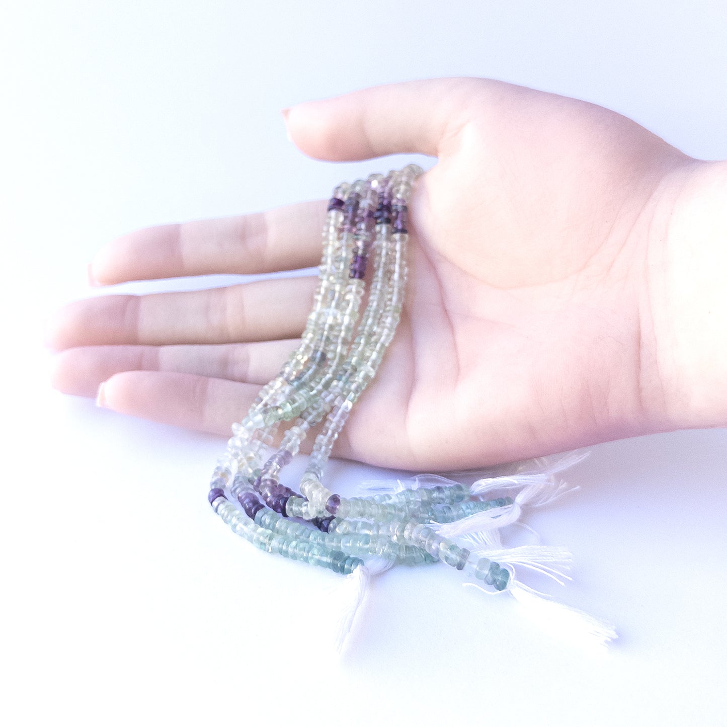 A person holds delicate strands of Fluorite beads, showcasing their smooth wheel design.