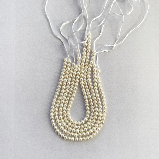 Dainty white freshwater pearls with a lustrous finish, neatly aligned for intricate designs.