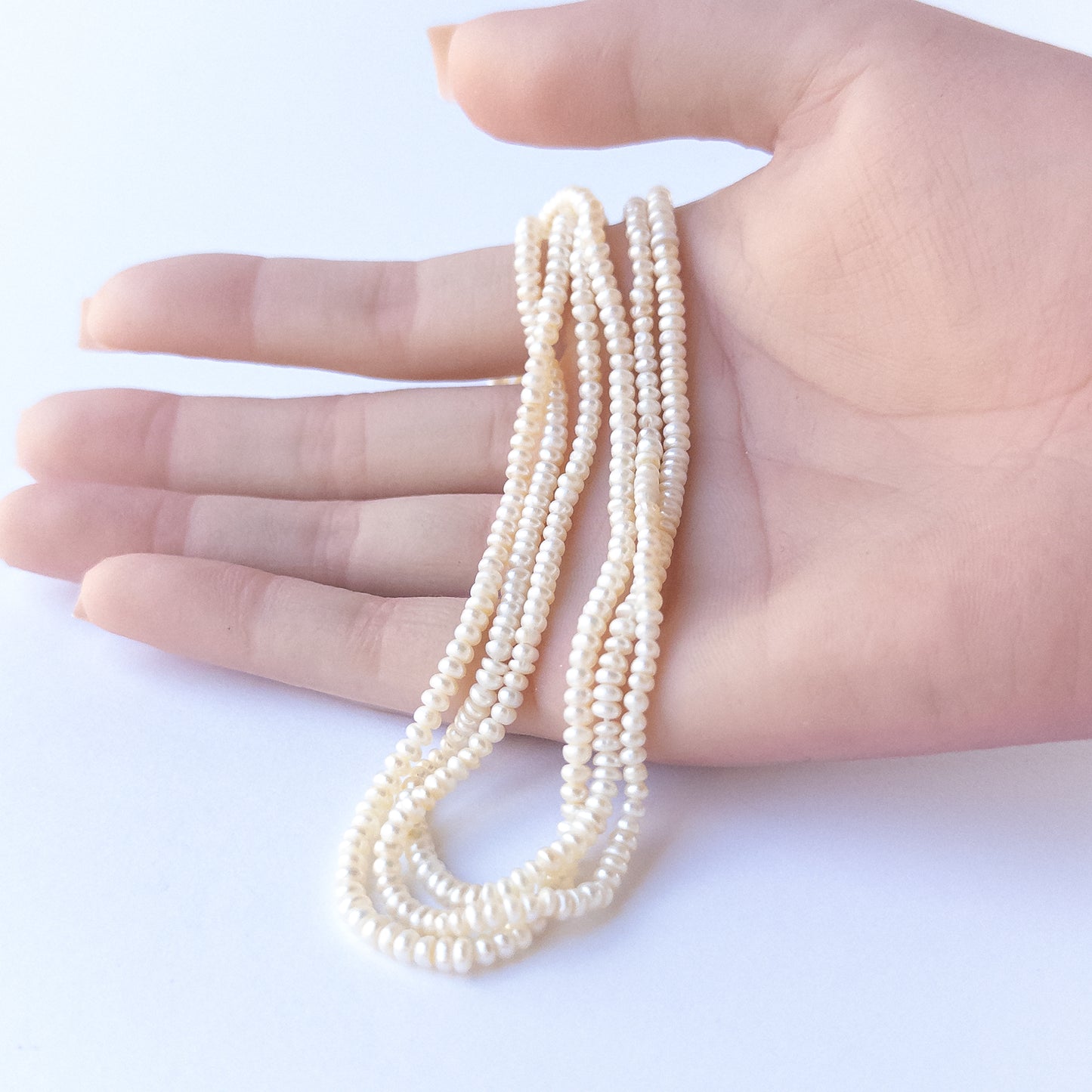 A person holds delicate strands of Freshwater Pearls beads, showcasing their rondelle design.