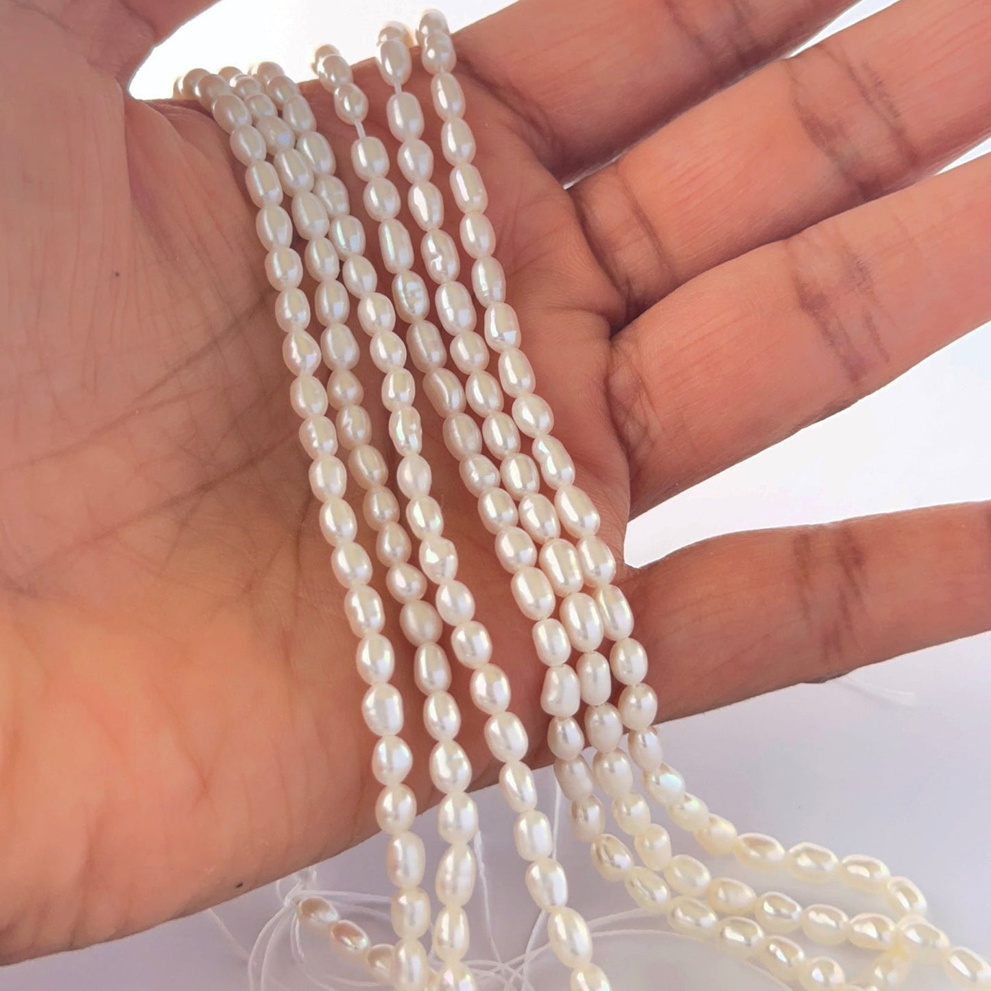 A person holds delicate strands of freshwater rice pearls, showcasing their natural shape.
