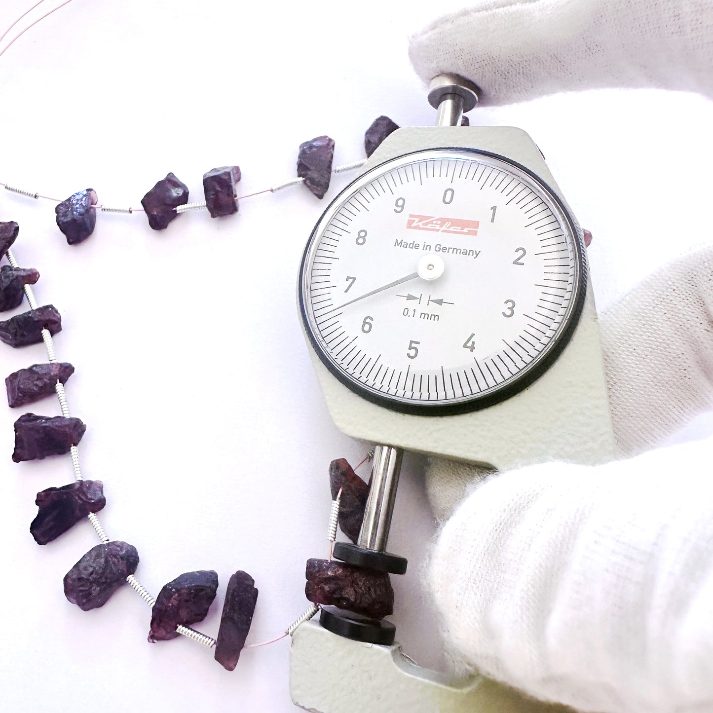 A dial gauge measures the Garnet side-drilled rough 6-7mm gemstone.