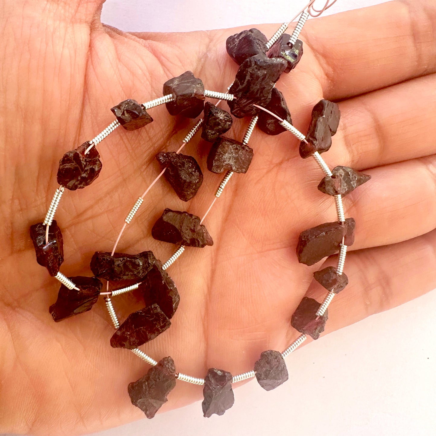 A person holds delicate strands of Garnet beads, showcasing their rough natural design.