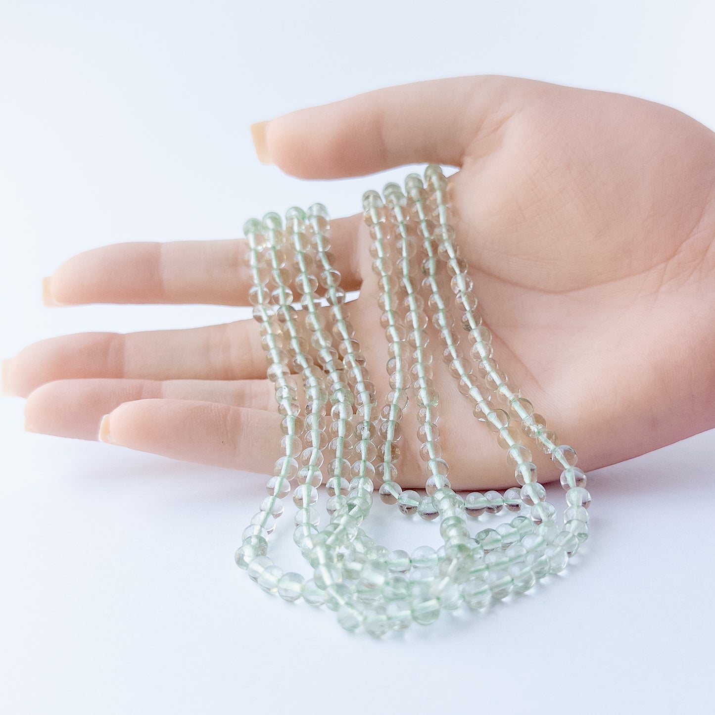 A person holds delicate strands of Green Amethyst beads, showcasing their smooth round design.