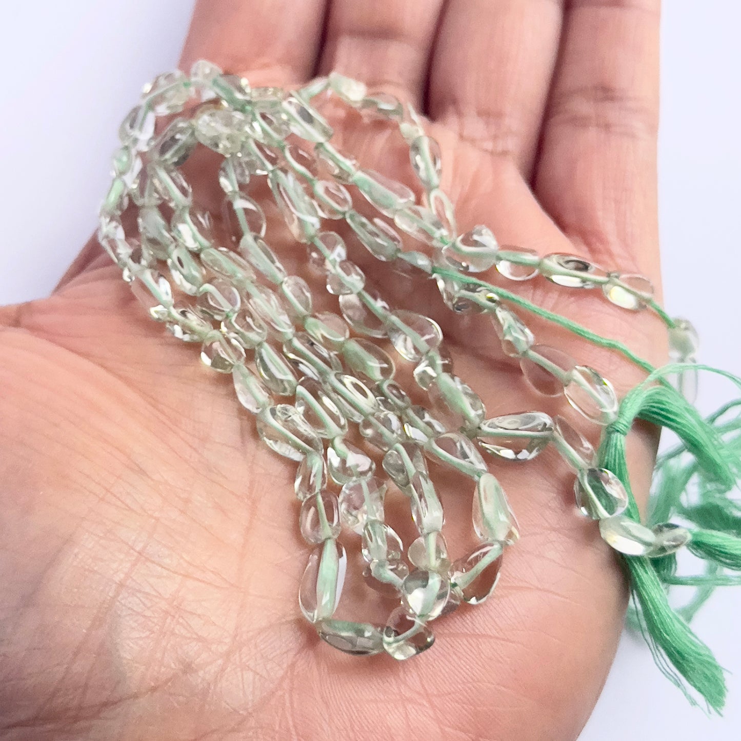 A person holds delicate strands of Green Amethyst beads, showcasing their smooth design.