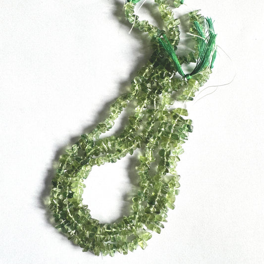 Green Apatite chips spread across a white surface, showcasing colour consistency and shape.