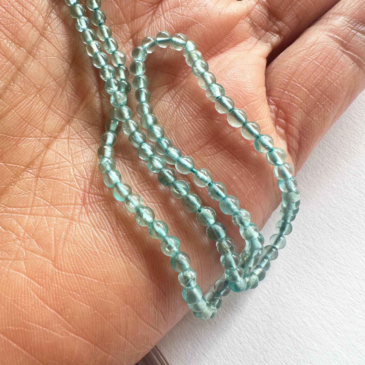 A person holds delicate strands of Green Apatite beads, showcasing their smooth design.