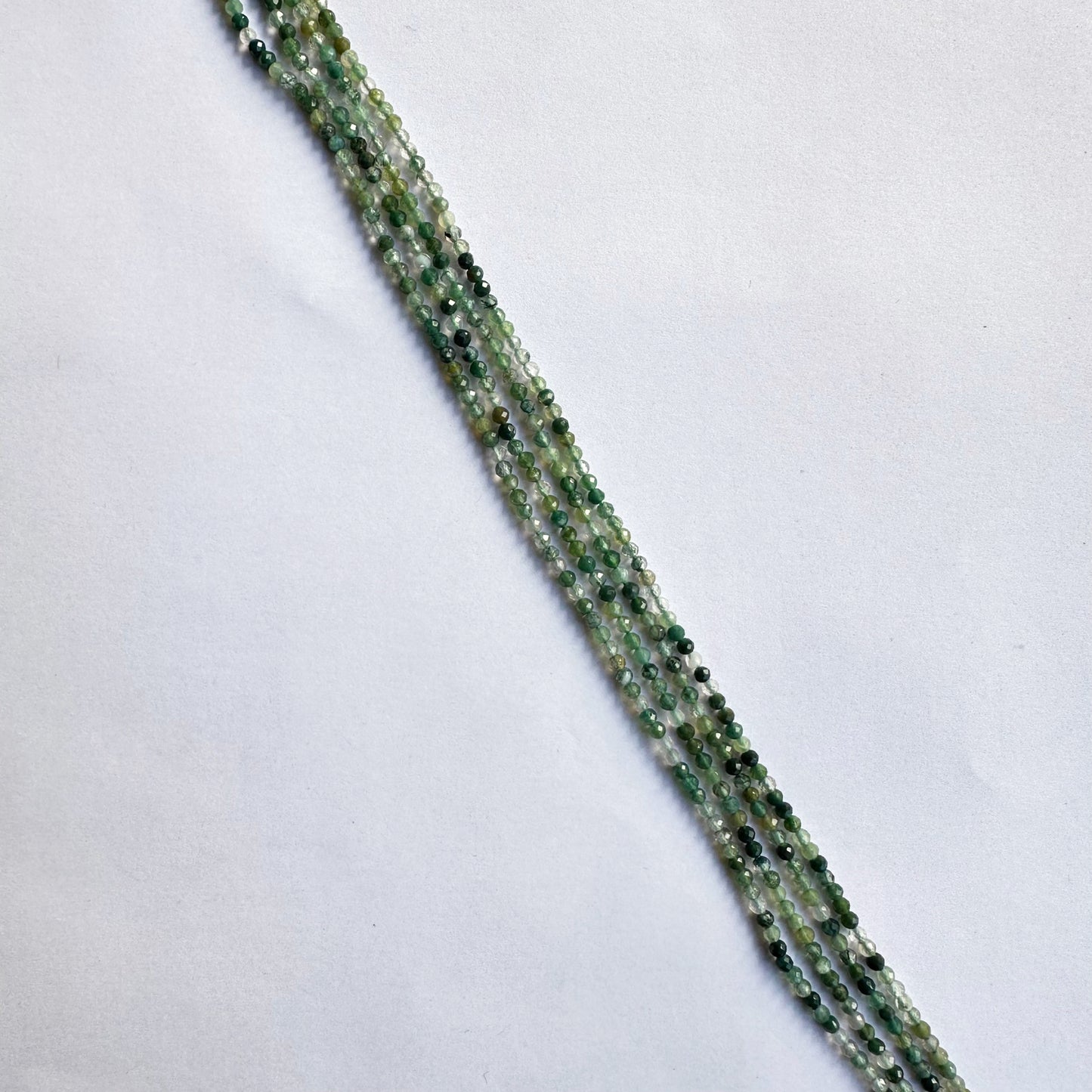 Strands of green aventurine beads coiled together, showing their soft green colour and faceted shine.