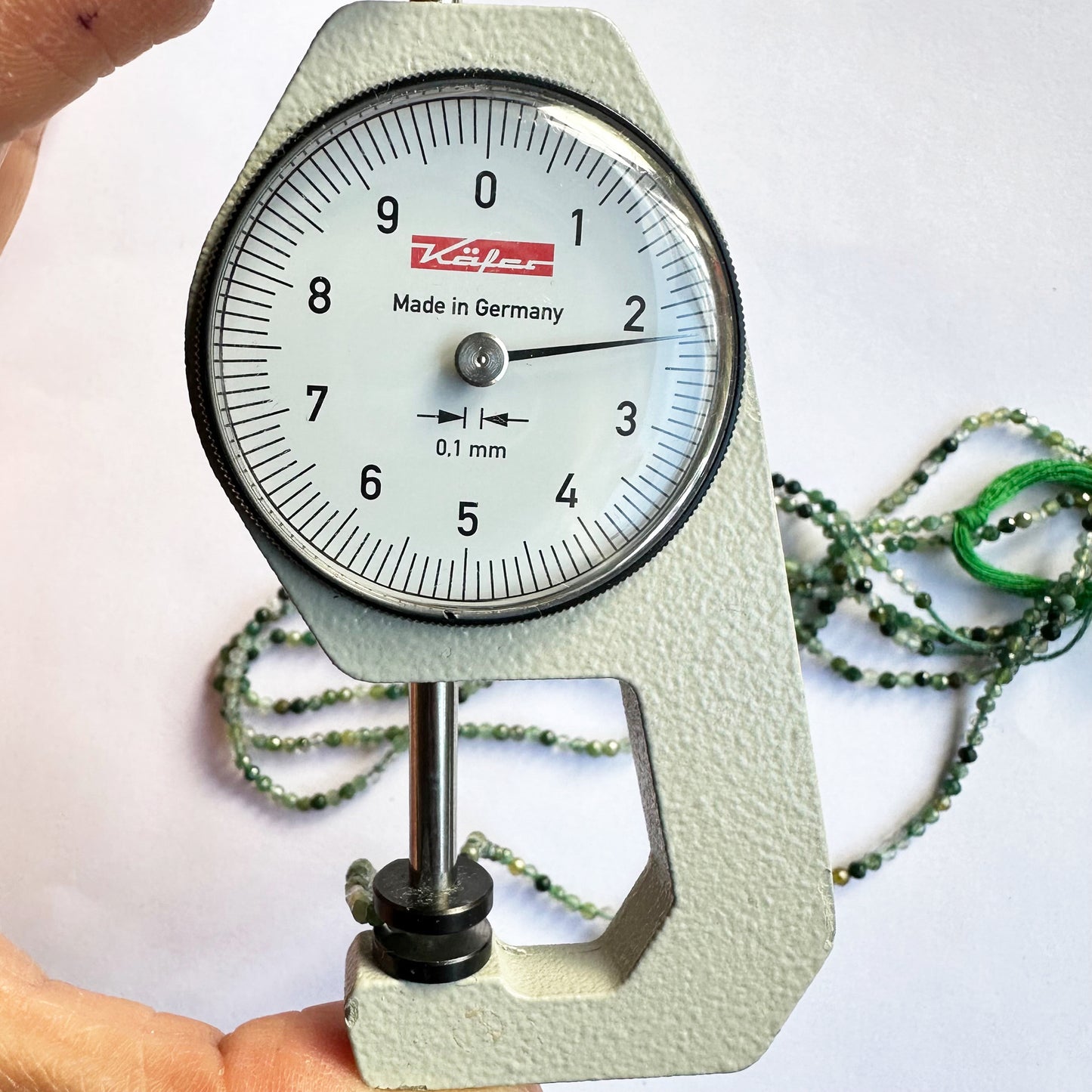 A dial gauge measures the green aventurine faceted rondelle 2.2-2.3mm gemstone for precision sizing.