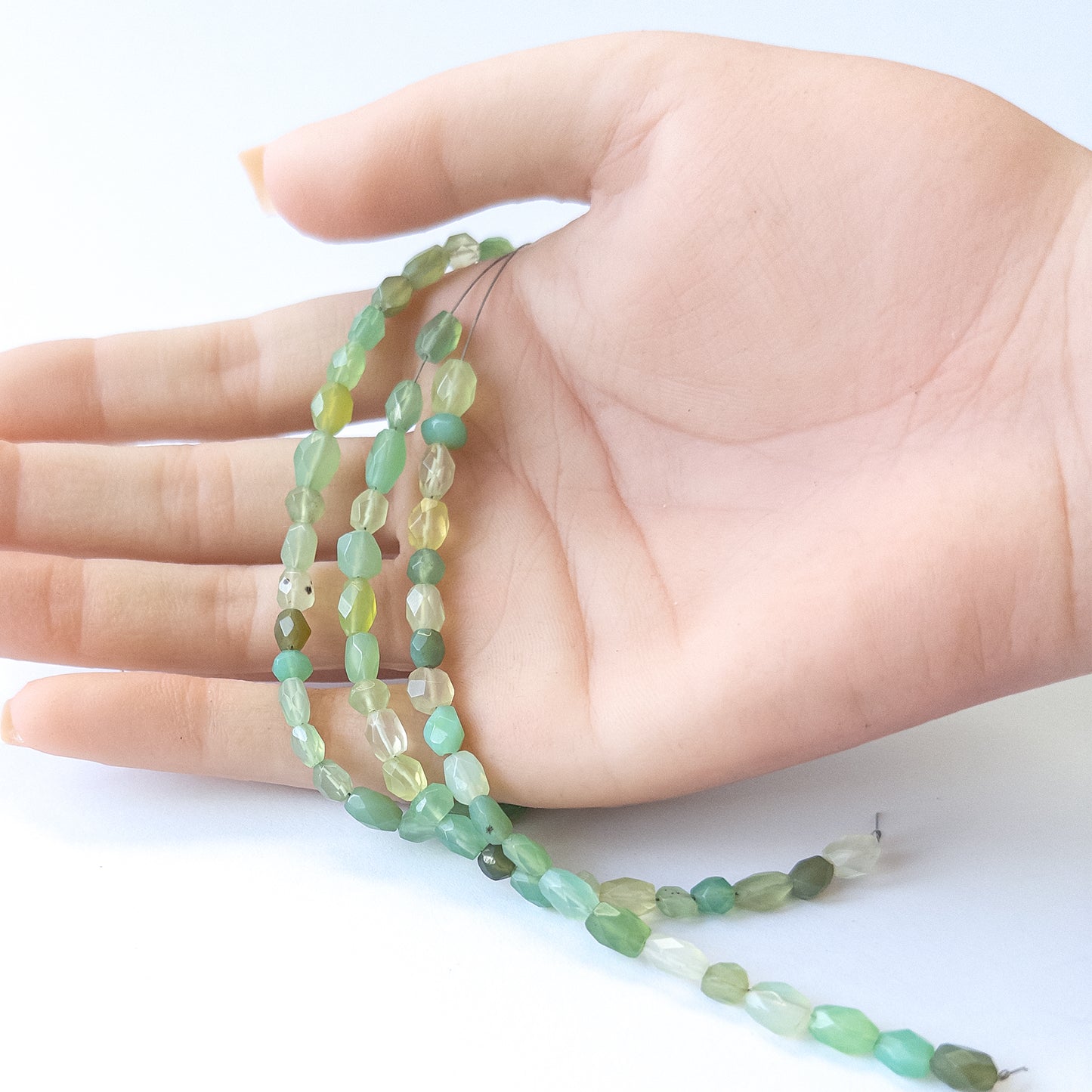 A person holds delicate strands of Green Chalcedony beads, showcasing their faceted oval design.