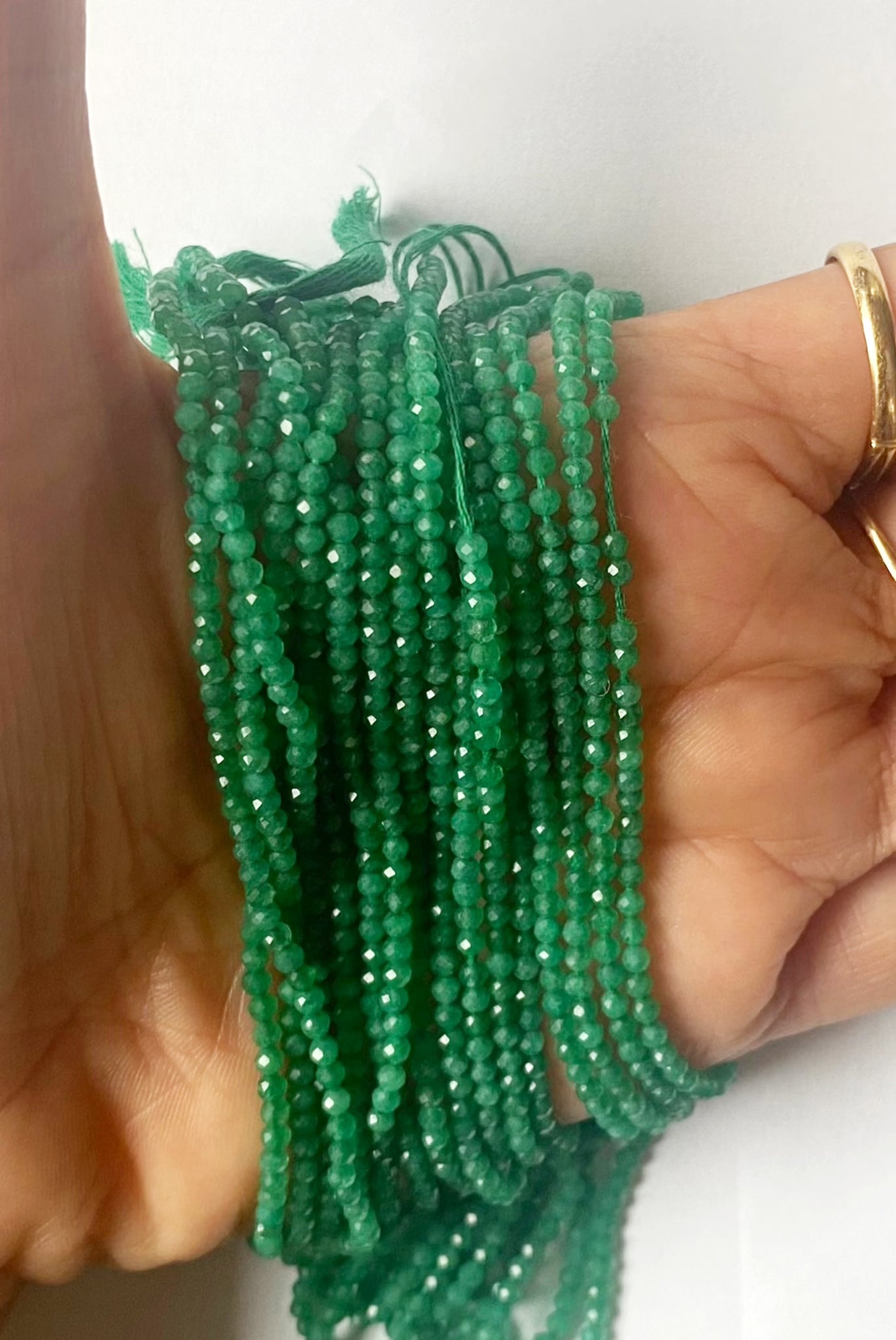A person holds delicate strands of Green Onyx beads, showcasing their smooth design.