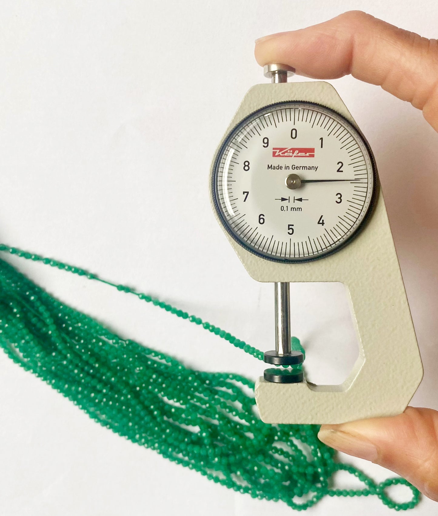 A dial gauge measures the Green Onyx micro-faceted rondelle beads, confirming their 2.4mm size.