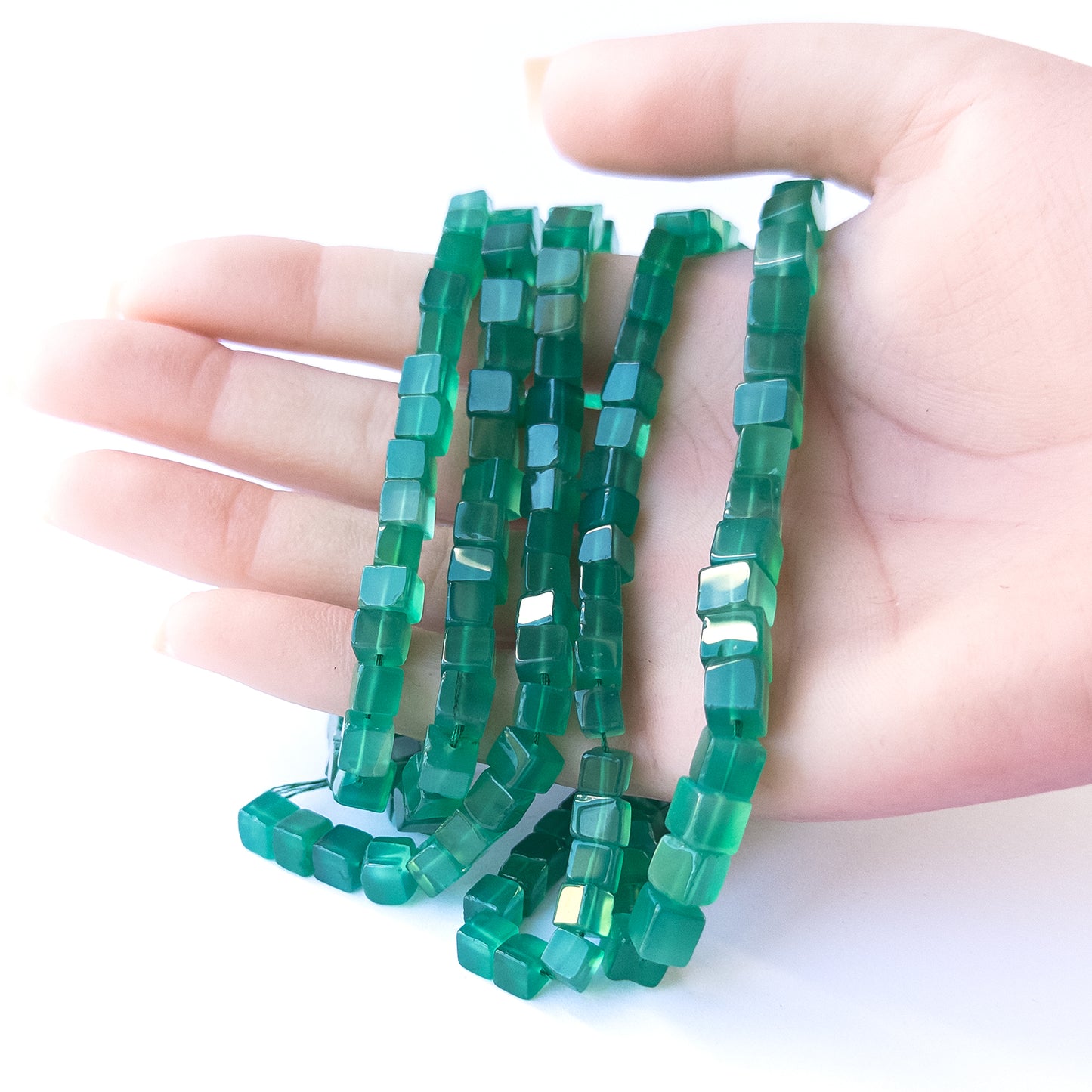 A person holds delicate strands of Green Onyx beads, showcasing their smooth cube design.