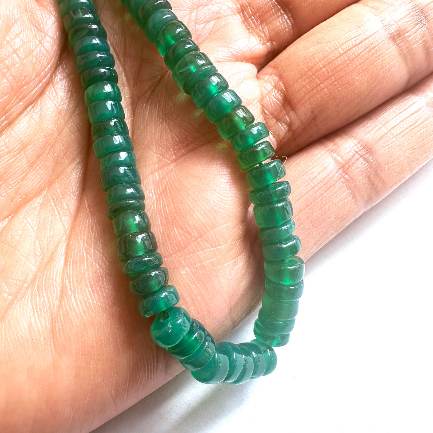 A person holds delicate strands of Green Onyx beads, showcasing their smooth design.
