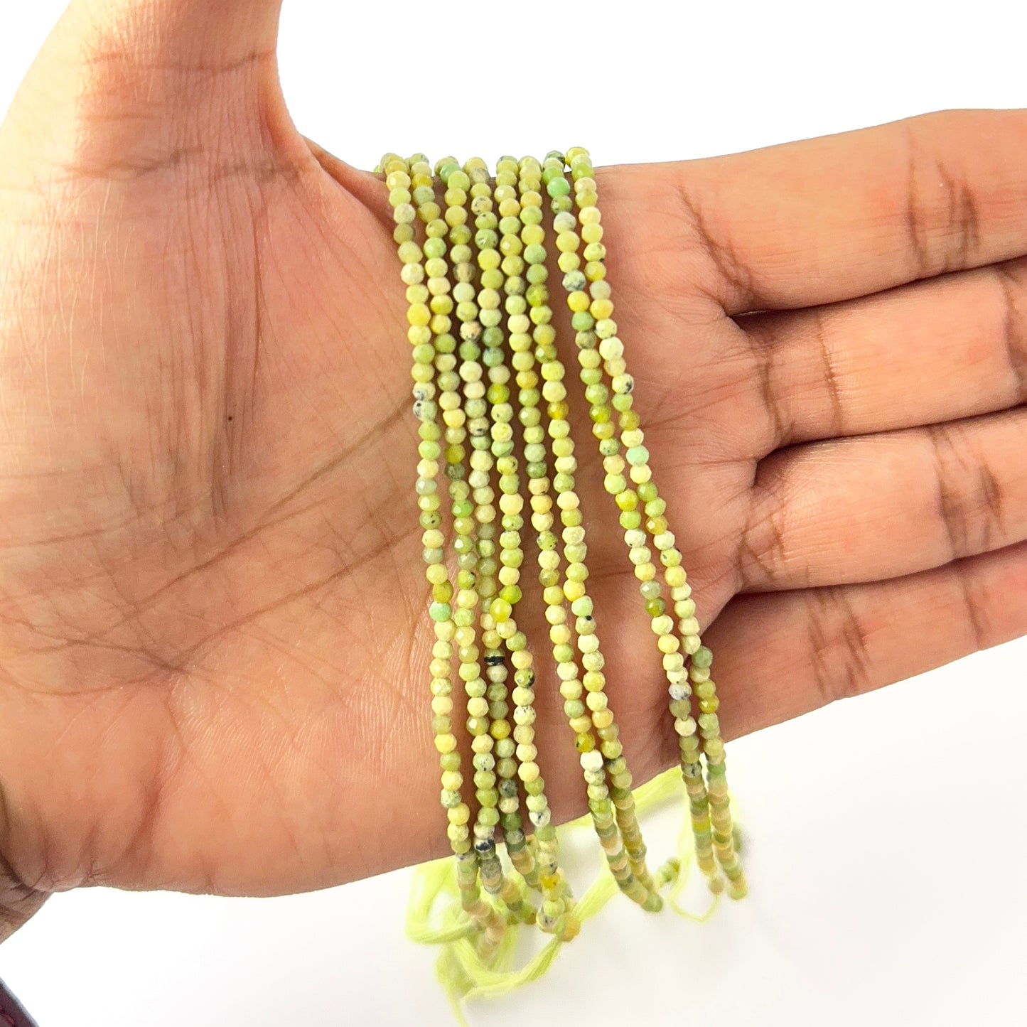 A person holds delicate strands of Green Opal beads, showcasing their faceted rondelle design.