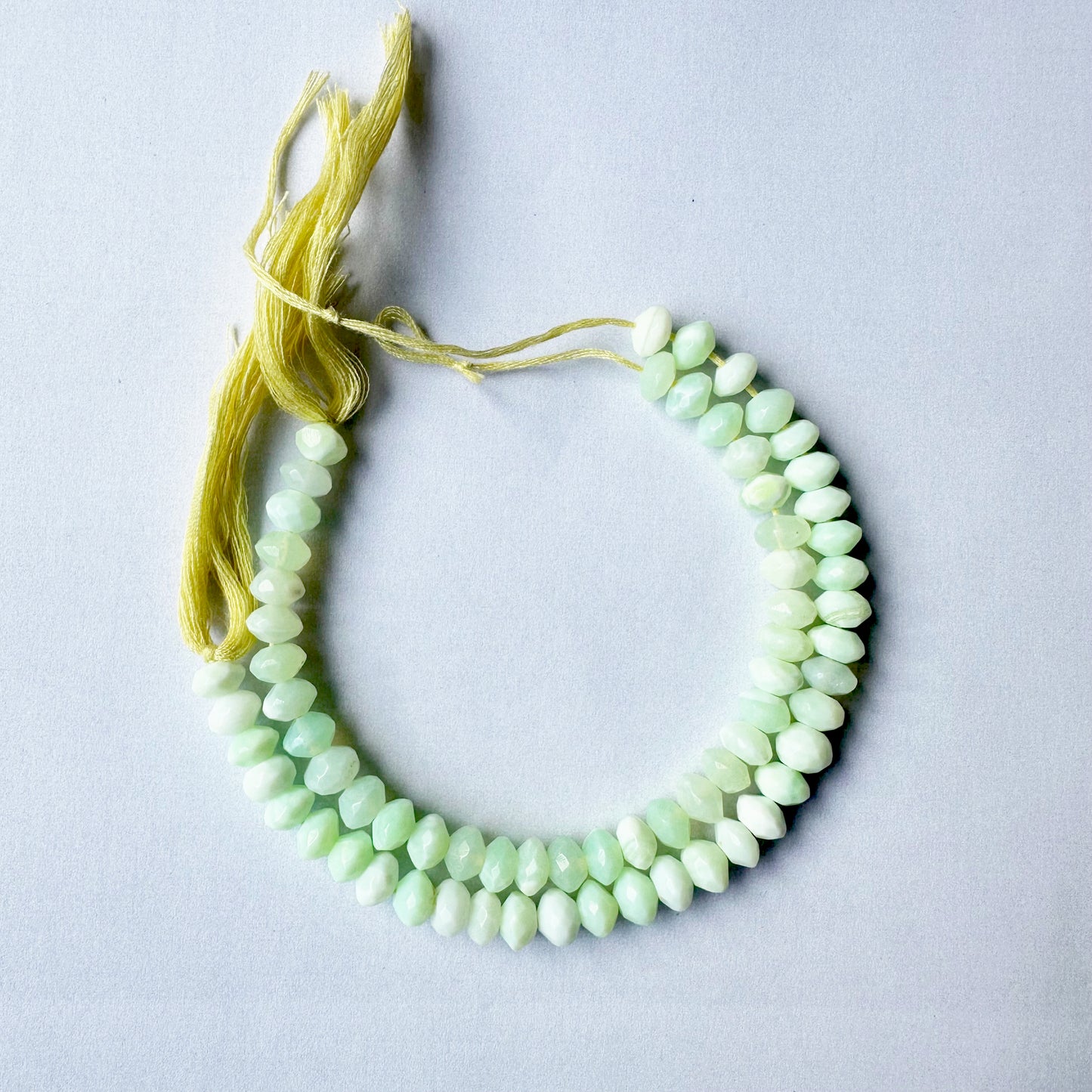 Light catches on Green Opal rondelle beads, highlighting their clarity and precision-cut edges.