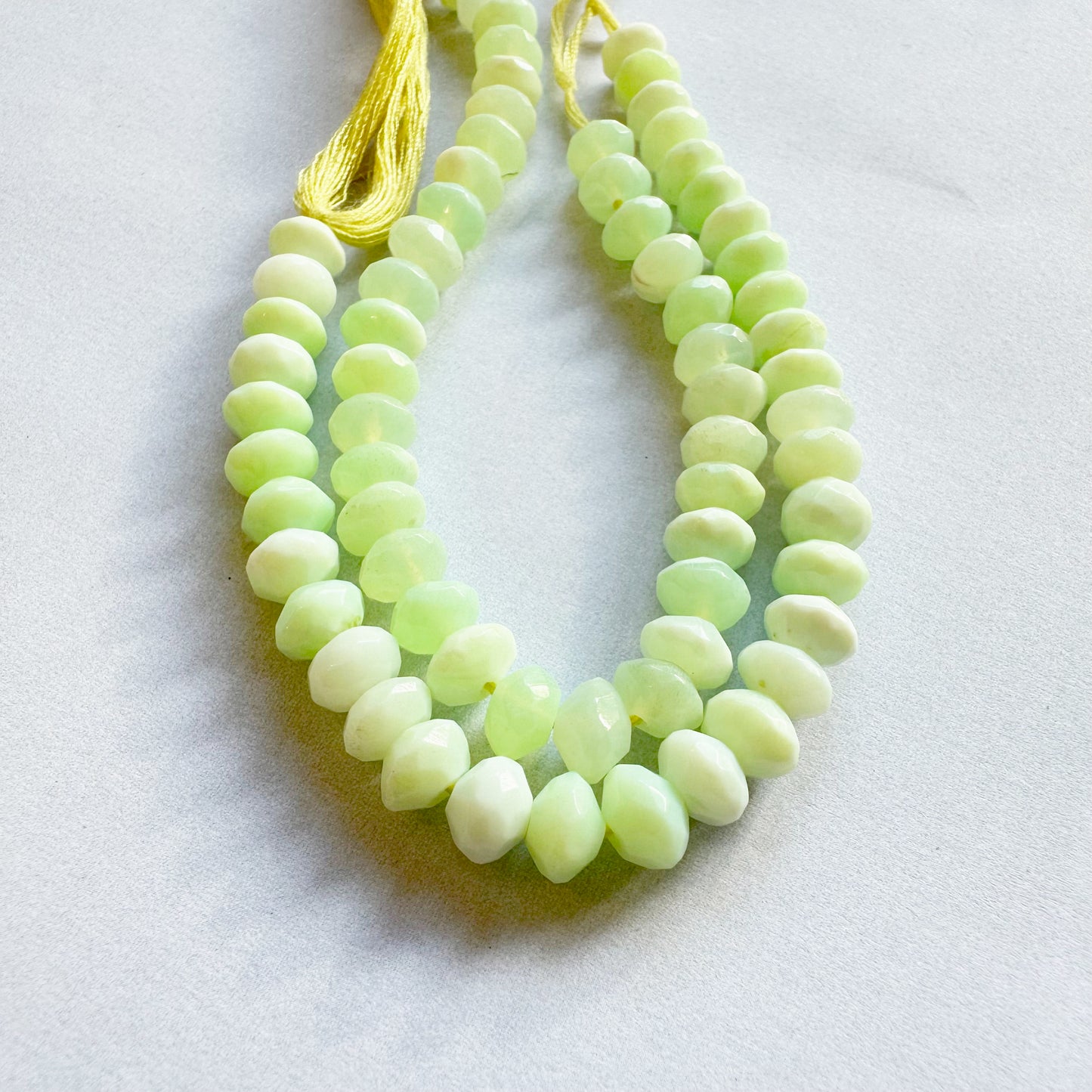 Neatly strung Green Opal faceted rondelles displayed in natural light.