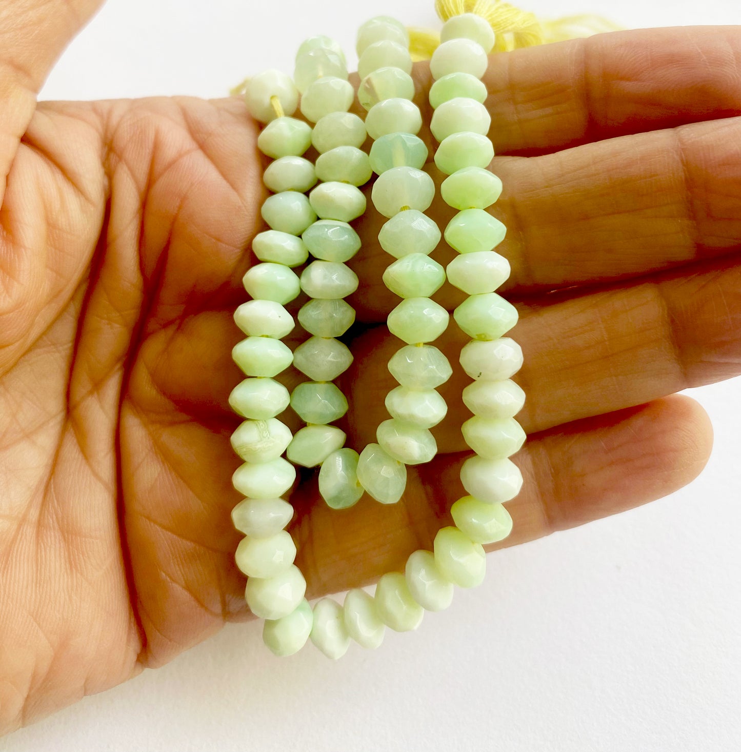 A person holds delicate strands of Green Opal beads, showcasing their rondelle design.