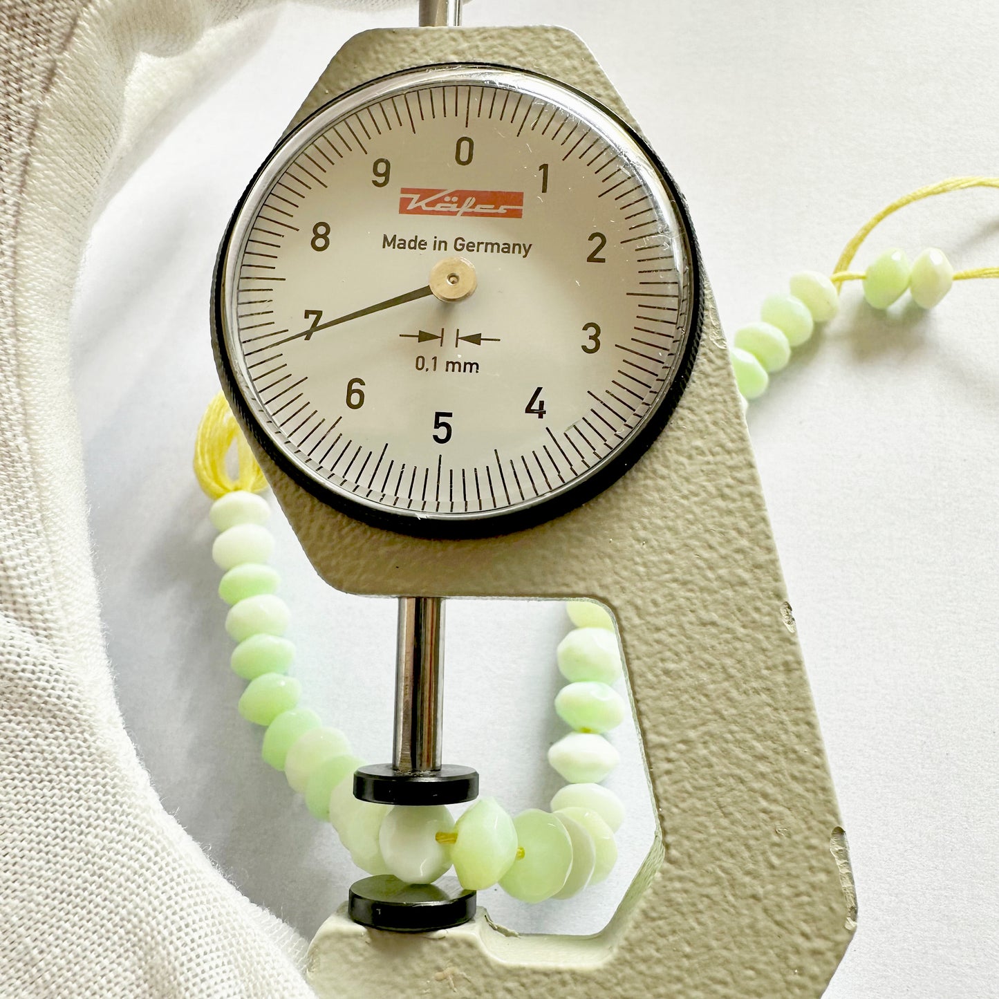 A dial gauge measures the Green Opal Faceted Rondelle 7mm gemstone.
