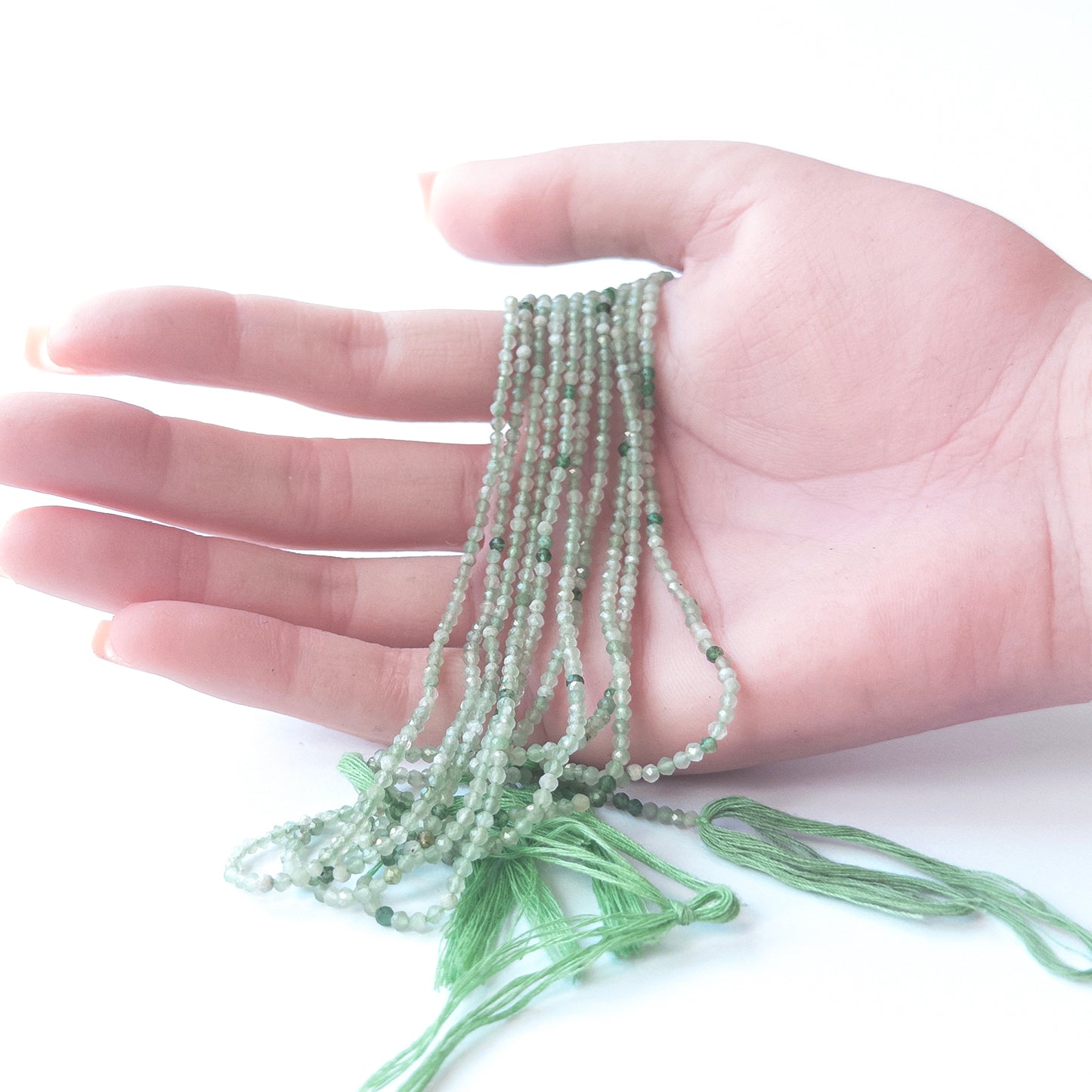 A person holds delicate strands of Green Shaded Chalcedony beads, showcasing their faceted rondelle design.
