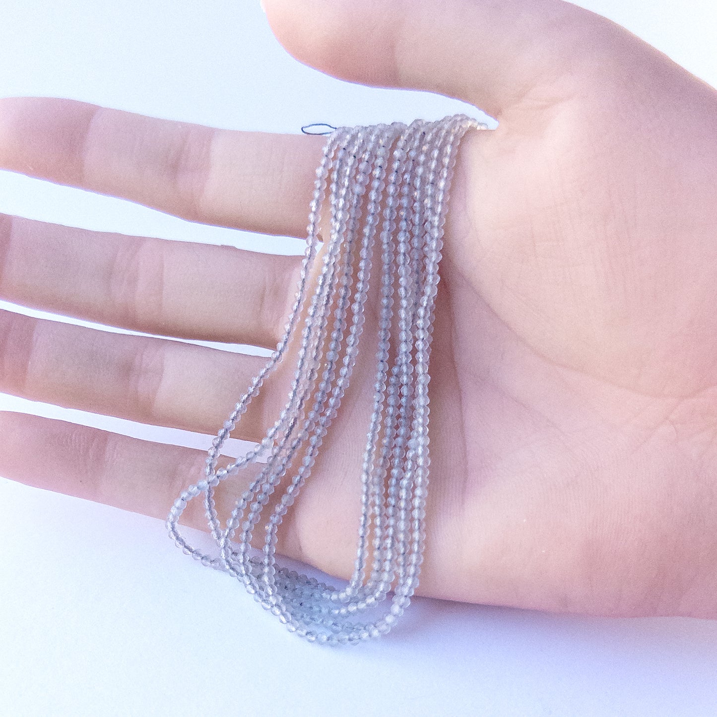 A person holds delicate strands of Grey Chalcedony beads, showcasing their faceted rondelle design.