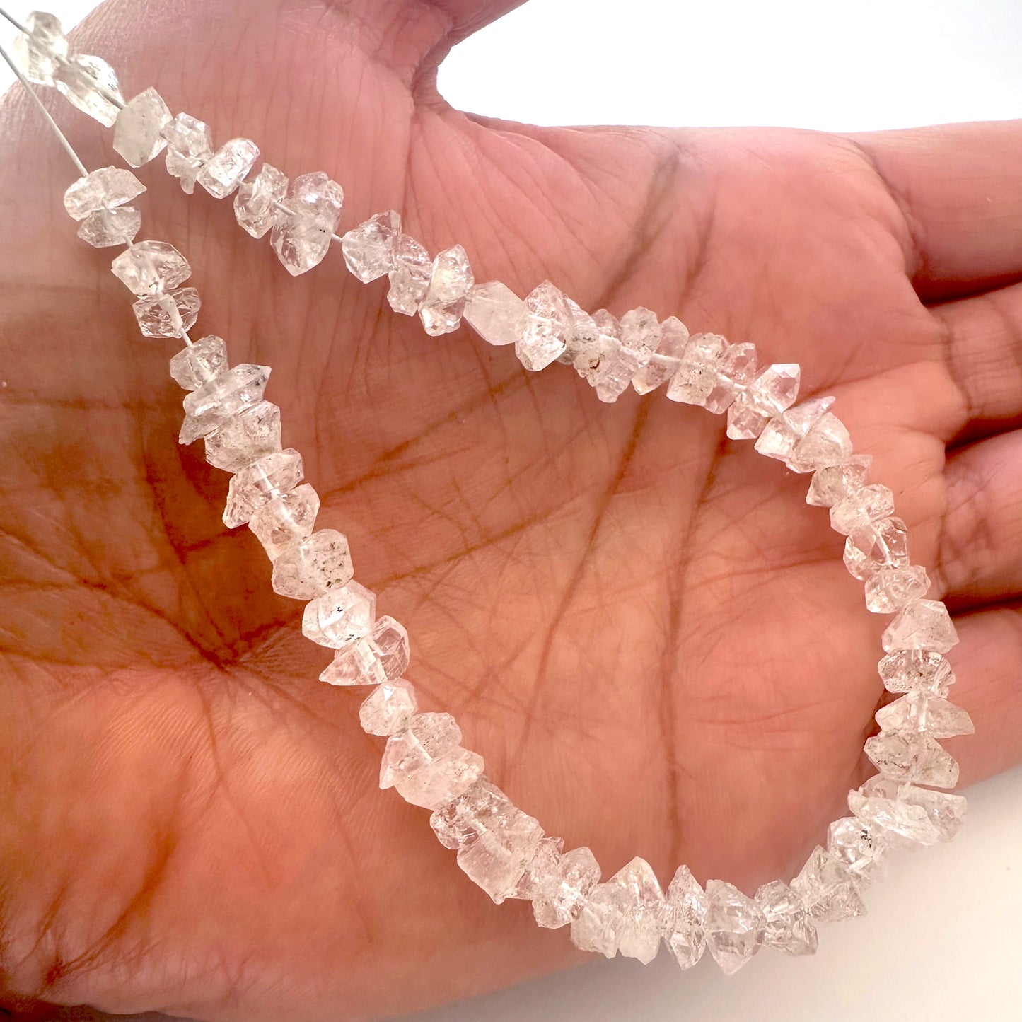 A person holds delicate strands of Herkimer Diamond beads, showcasing their smooth design.