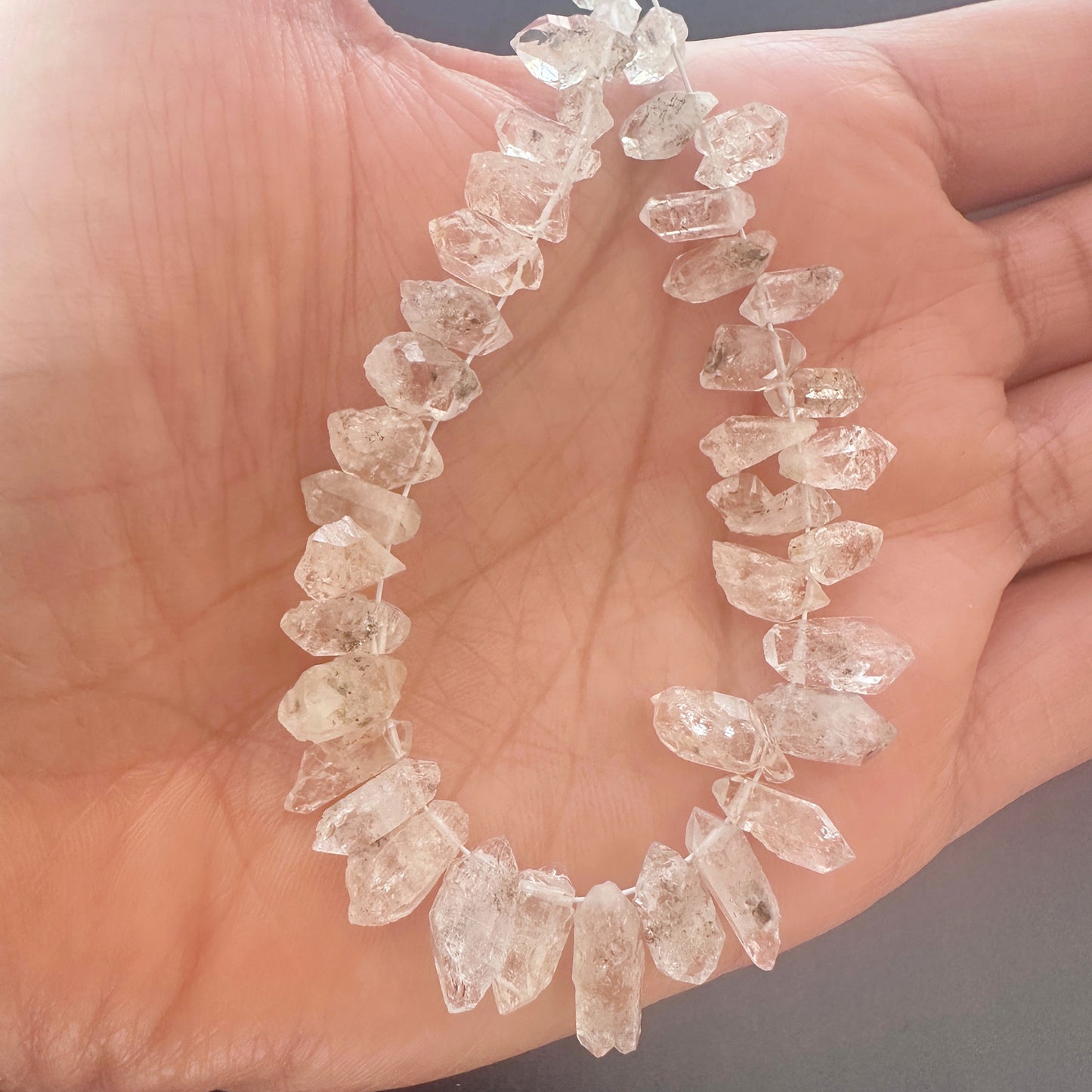 A person holds delicate strands of Herkimer beads, showcasing their rough design.