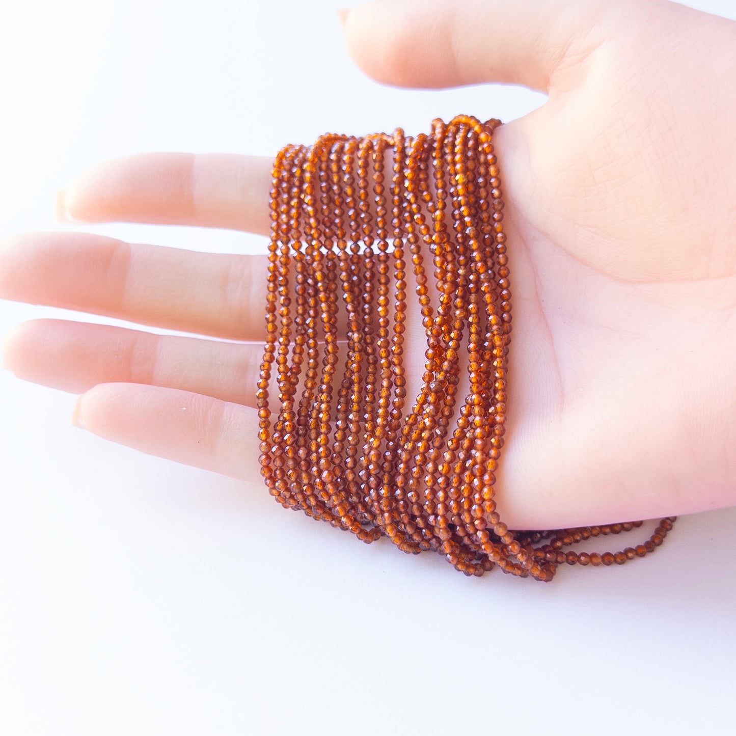 A person holds delicate strands of Hessonite beads, showcasing their faceted rondelle design.