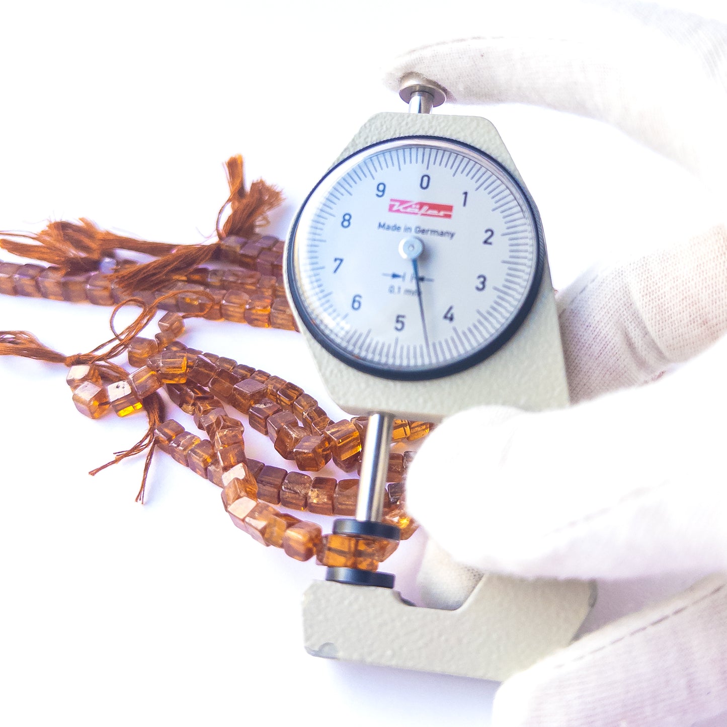 A dial gauge measures the Hessonite smooth cube 5mm gemstone.