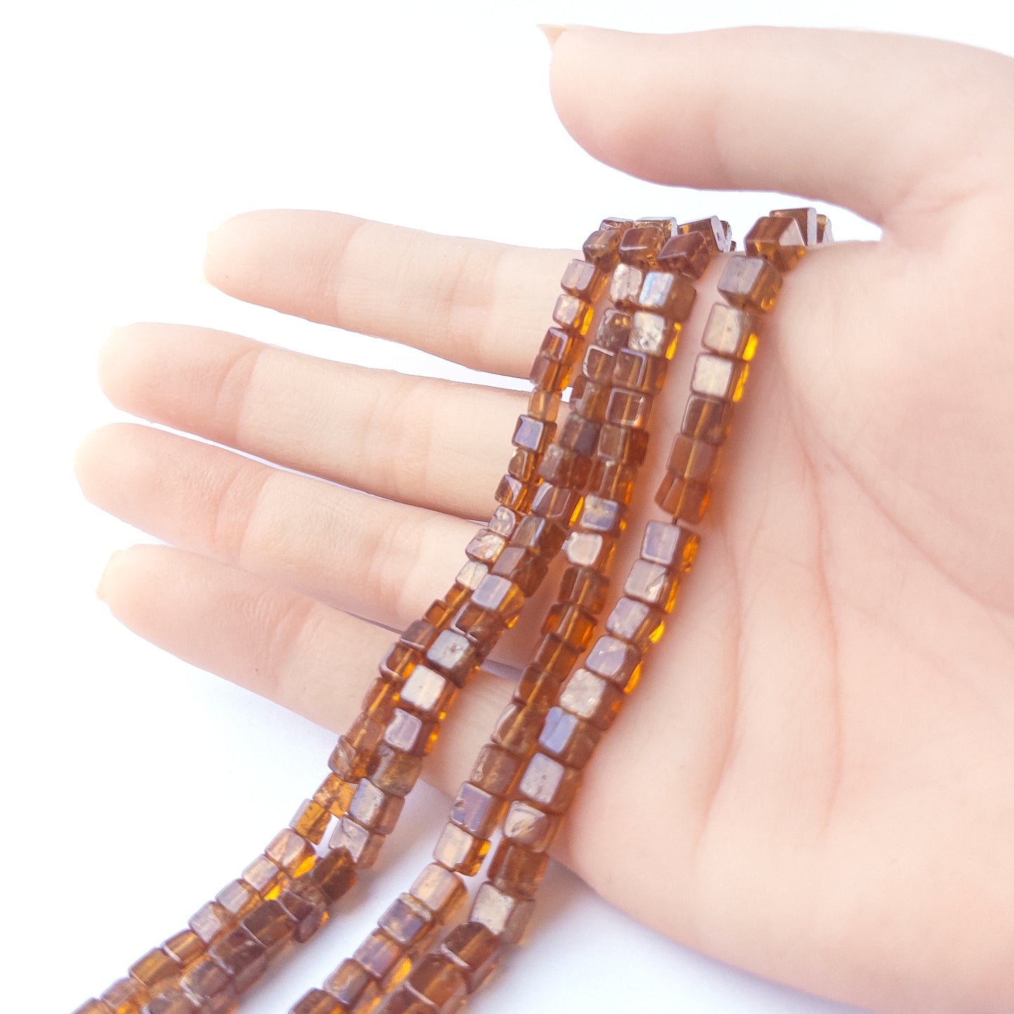 A person holds delicate strands of Hessonite beads, showcasing their smooth cube design.