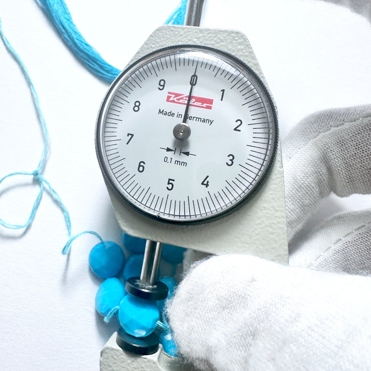A dial gauge measures the Howlite Turquoise faceted round 10mm gemstone.