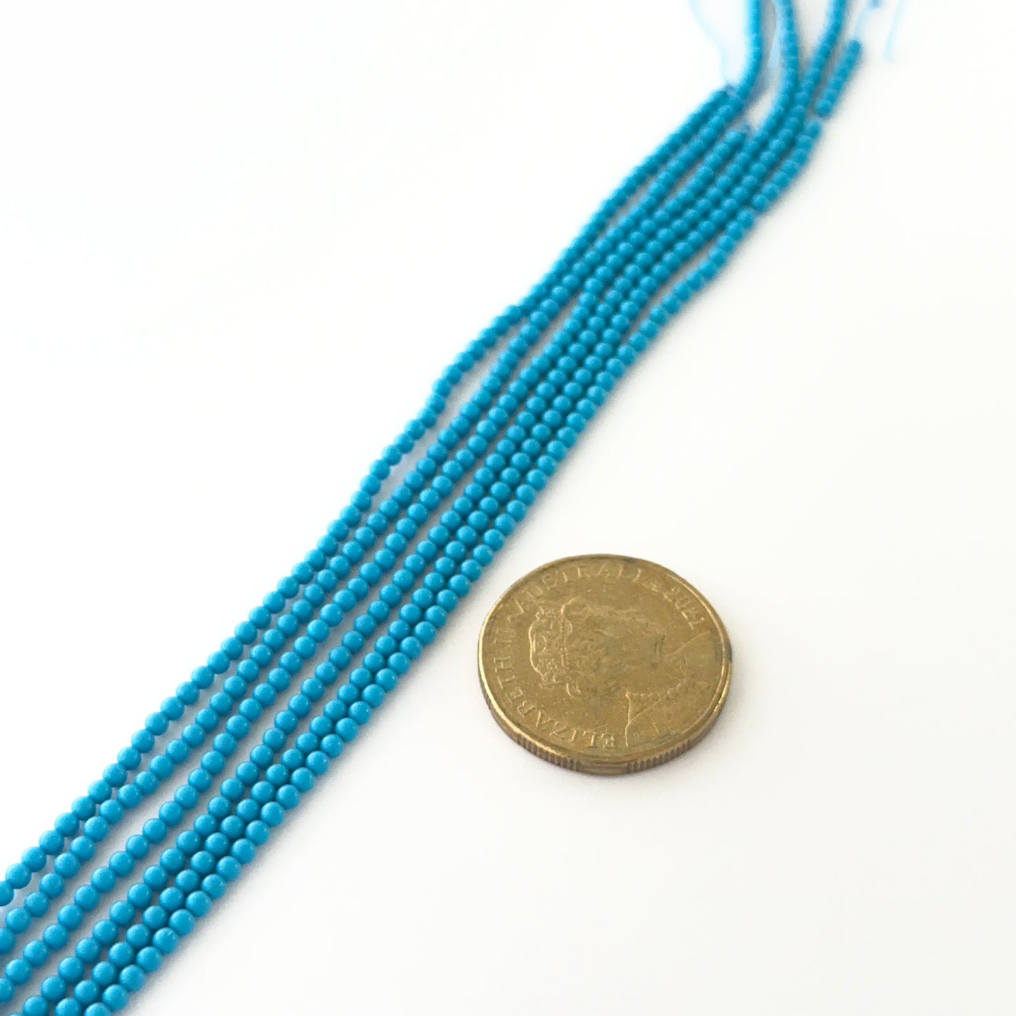 A coin is placed near delicate strands of Howlite Turquoise beads for scale