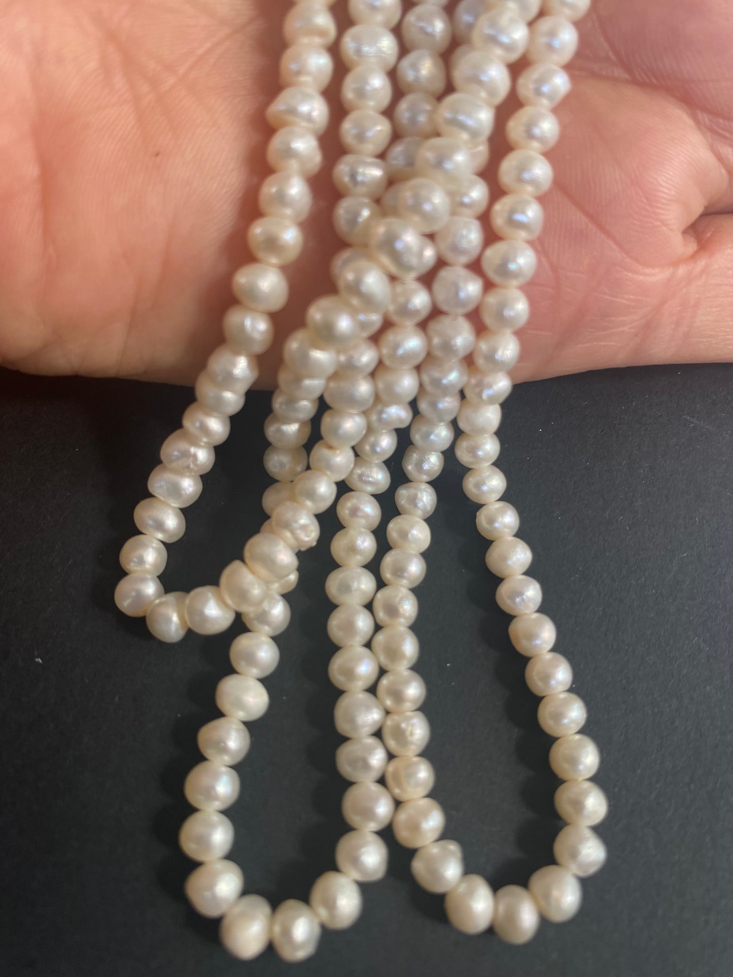 A hand grips a beautiful strand of 5.5-6mm freshwater rice pearls, highlighting their smooth texture and shine.