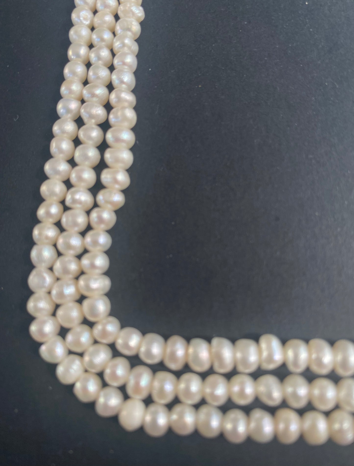 Multiple beautiful strands of 5.5mm-6mm freshwater rice pearls resting on a sleek black background, showcasing their lustre.
