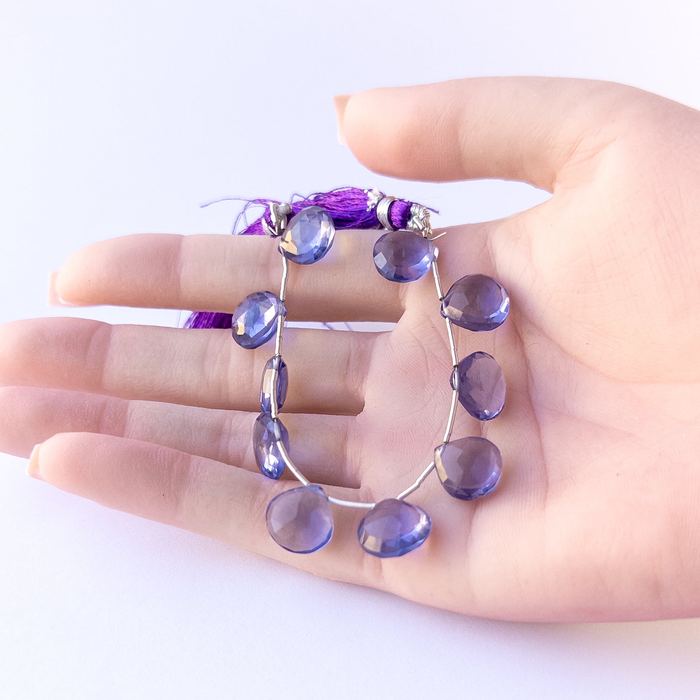 A person holds delicate pieces of Hydro beads, showcasing their faceted briolette design.