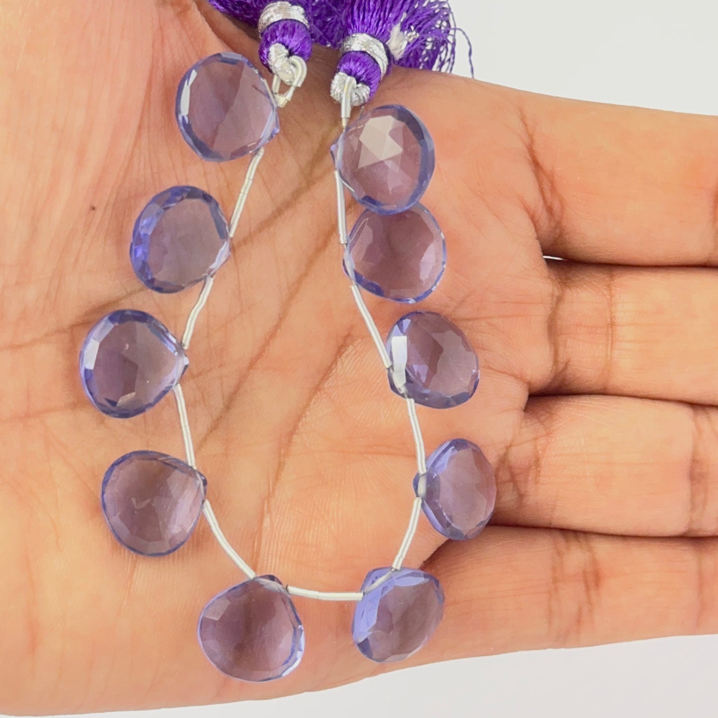 A person holds delicate strands of Hydro beads, showcasing their faceted briolette design.