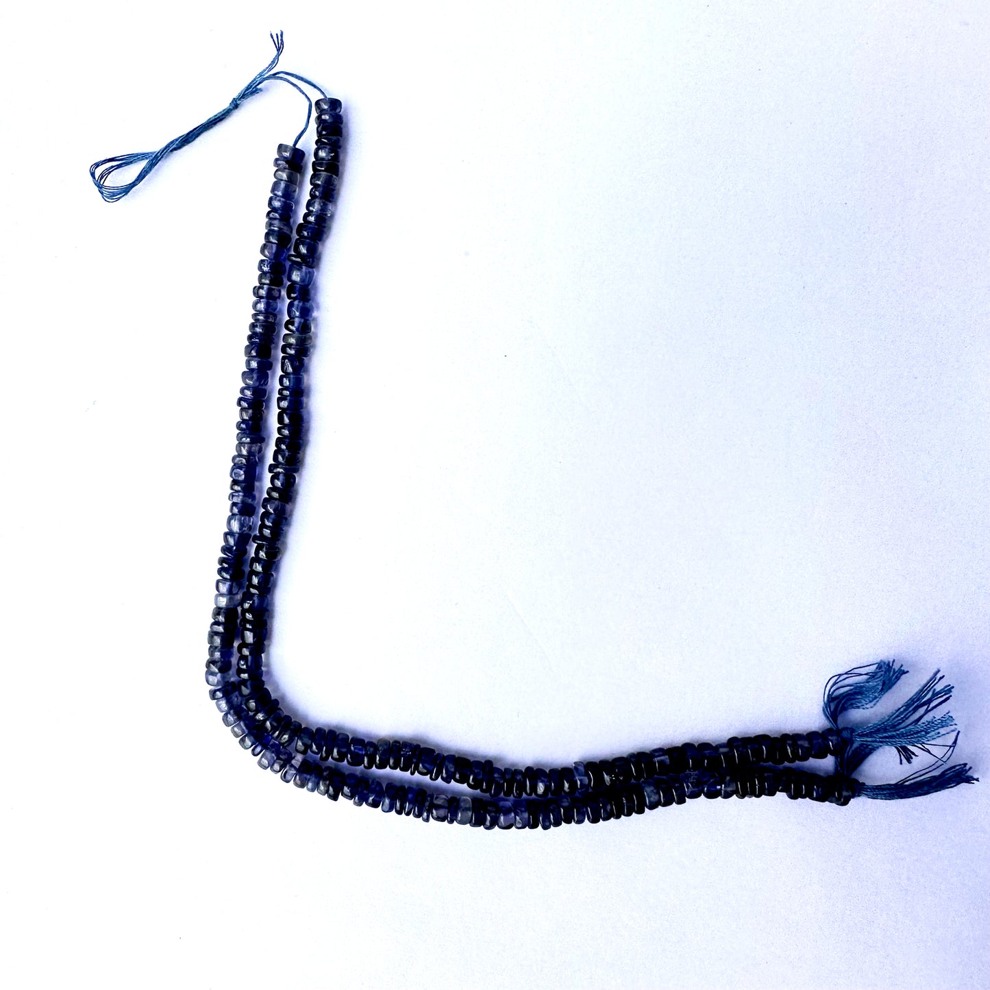 Close-up of Iolite gemstone beads arranged in a 21cm strand with smooth wheel cut.