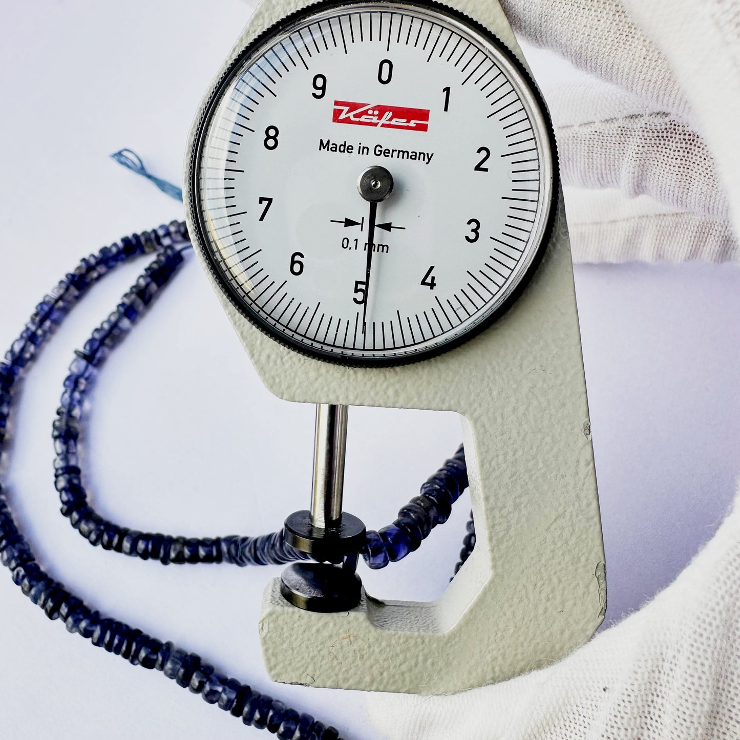 A dial gauge measures the Iolite smooth wheel 4.7–5mm gemstone.